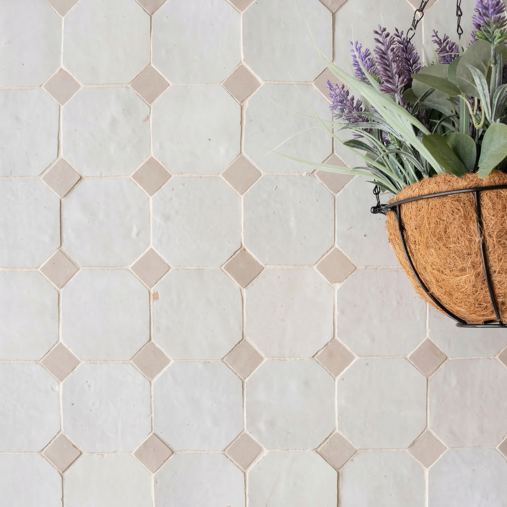 Soft white ceramic tiles with small ecru diamond details forming a geometric pattern alongside a hanging planter with purple flowers