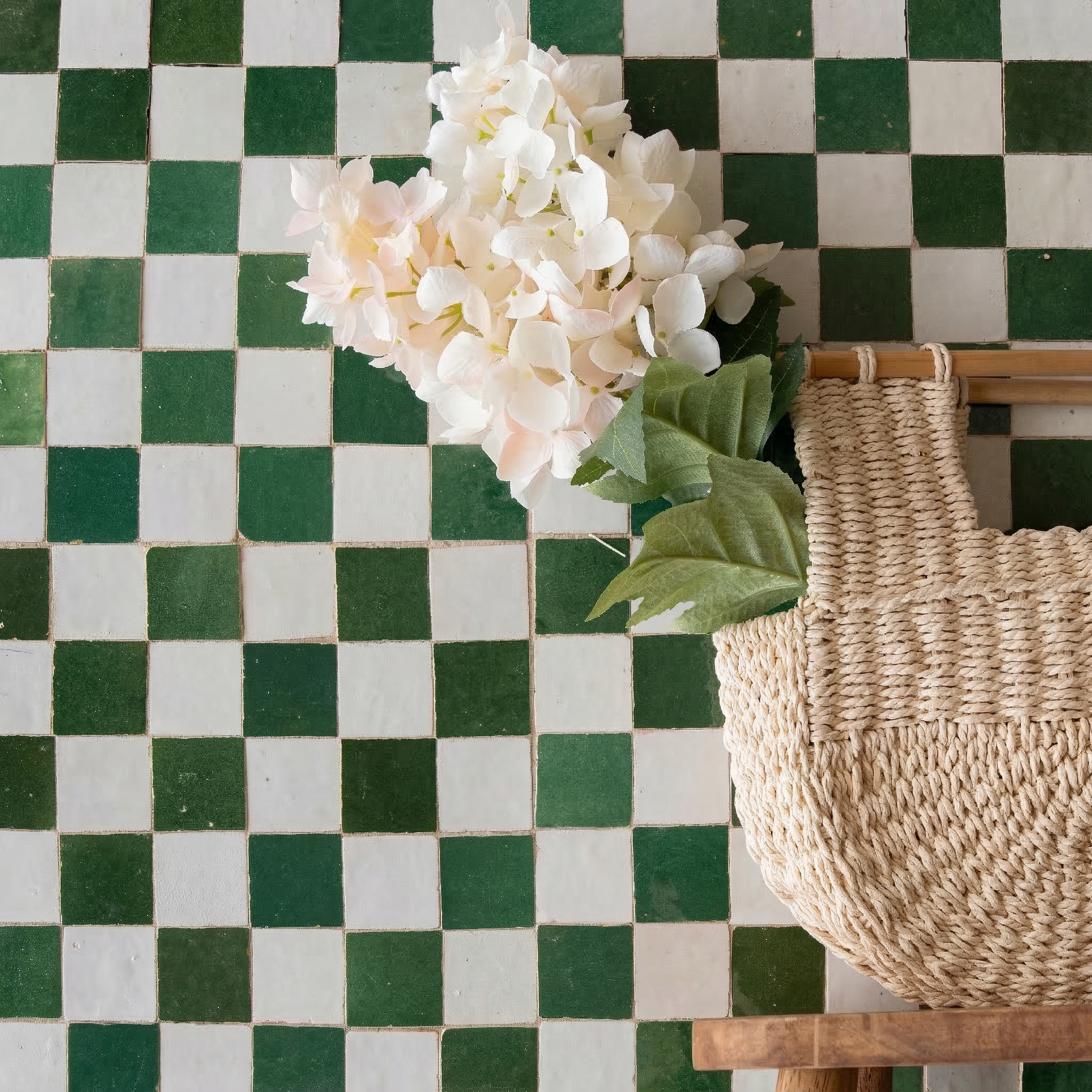 Checkerboard mosaic of jade green and white square ceramic tiles with a woven basket and pale hydrangea flowers nearby