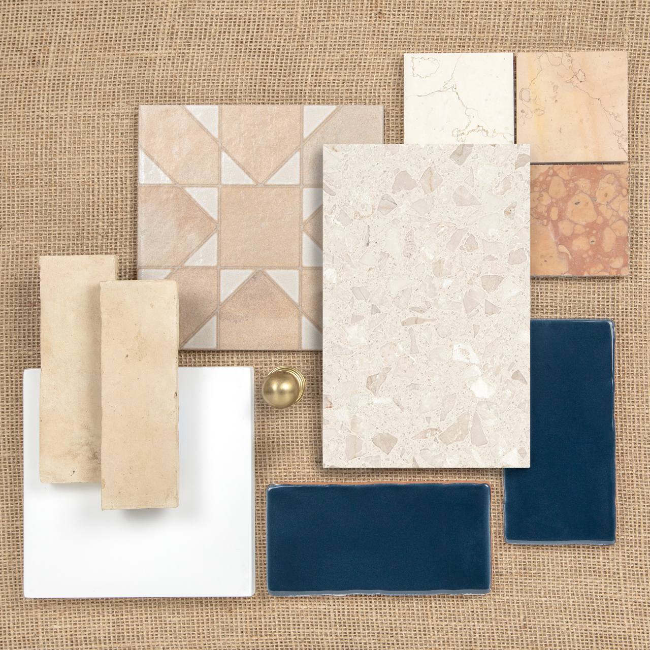 Assorted tile samples in cream, blue, and terracotta tones arranged on burlap, including geometric and terrazzo designs