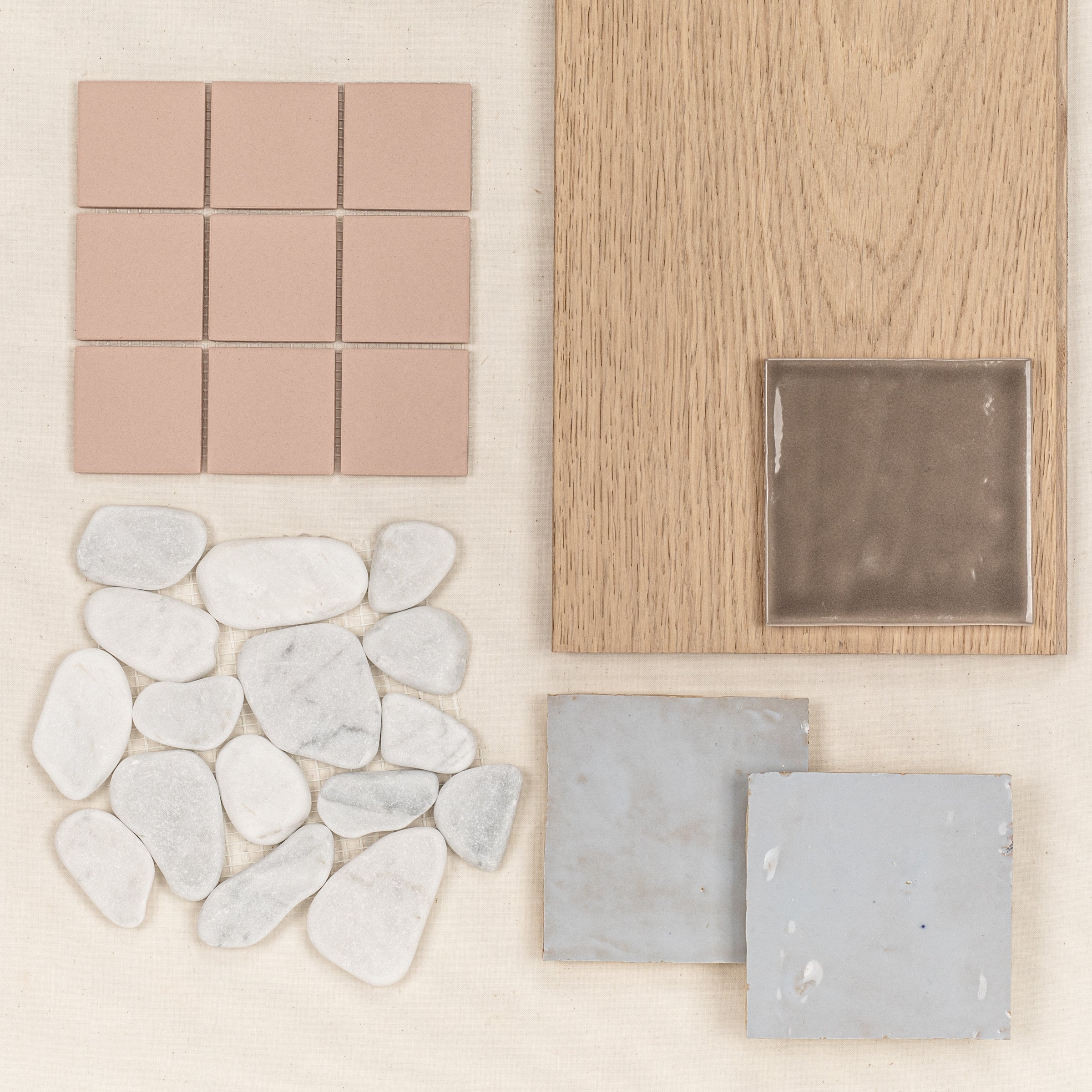 Arrangement of soft pink ceramic tiles, natural white stone pebbles, light wood, and glossy gray ceramic tiles on a neutral surface