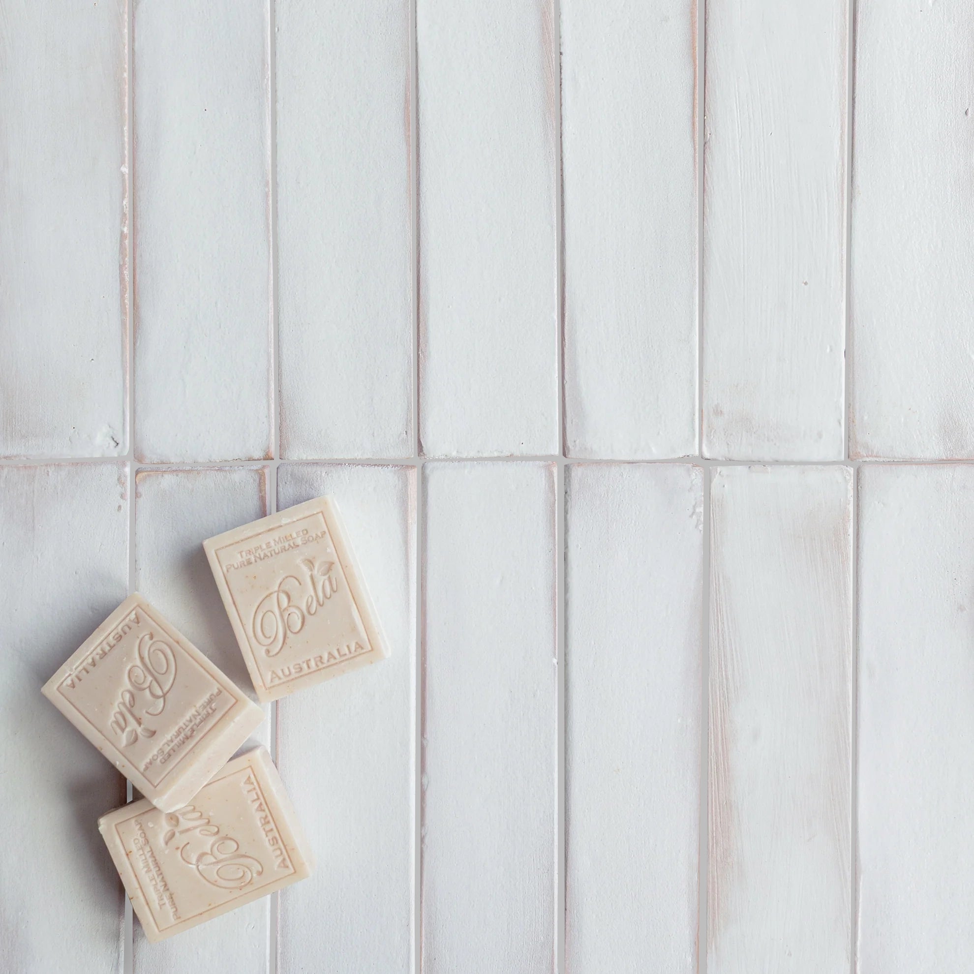 Glazed white ceramic tile strips with soft beveled edges paired with three vintage-style beige soap bars