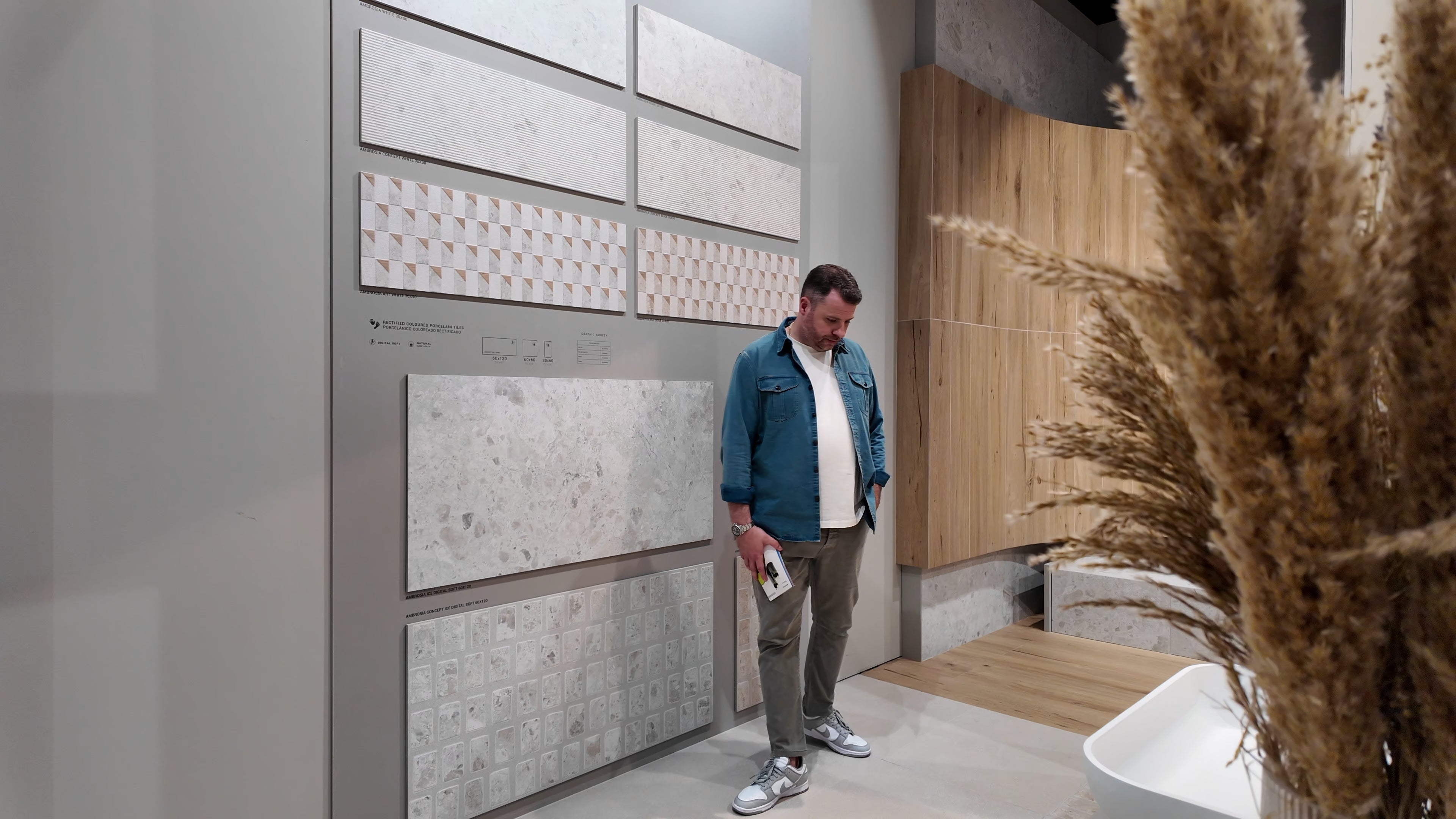 Man examining large format ceramic tile samples displayed on a gray wall in a modern showroom setting