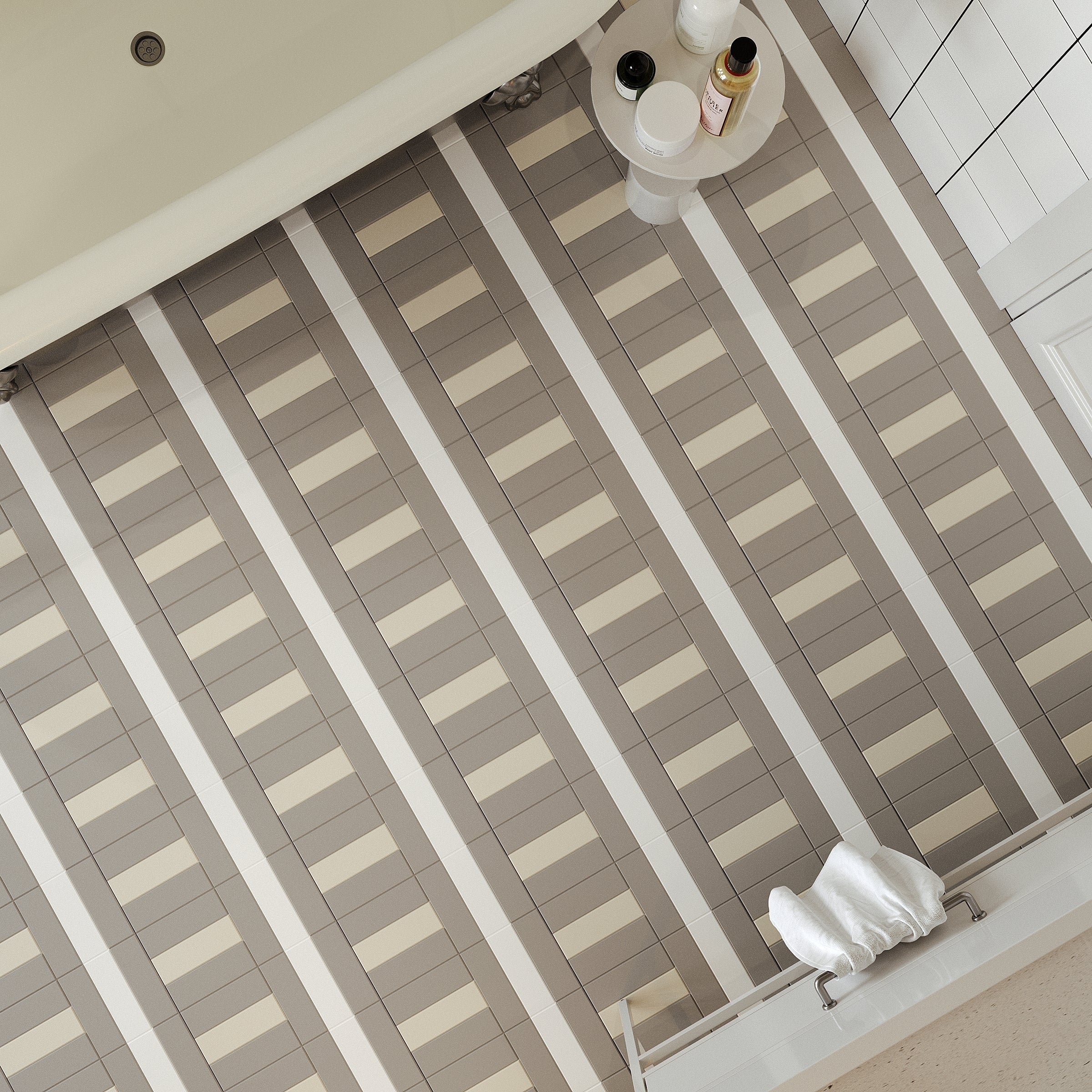 Top-down view of bathroom floor with rectangular ceramic tiles in beige and taupe stripes beside white tiled wall and bathtub