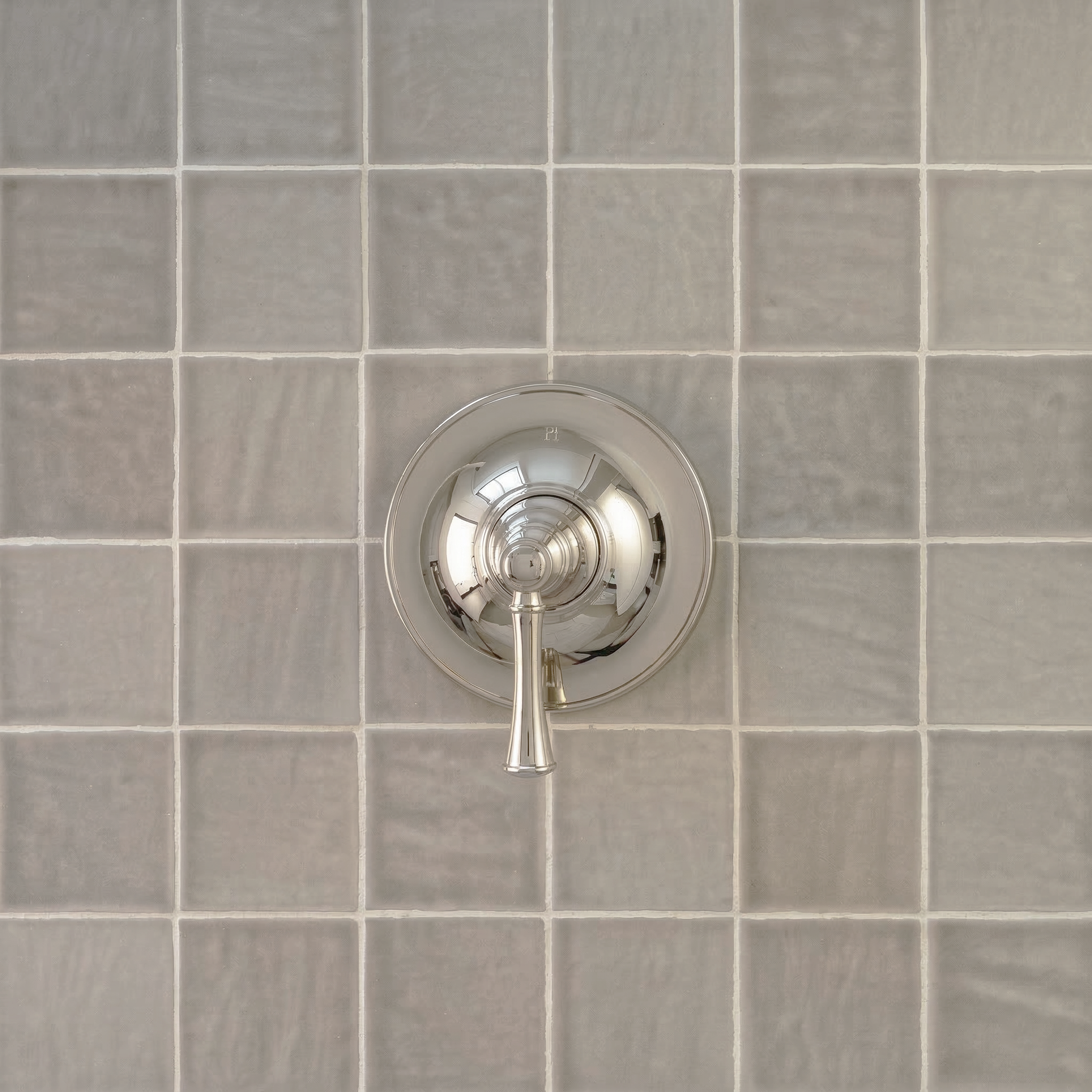 Matte gray ceramic tiles with slight surface texture forming a grid around a polished chrome shower handle fixture