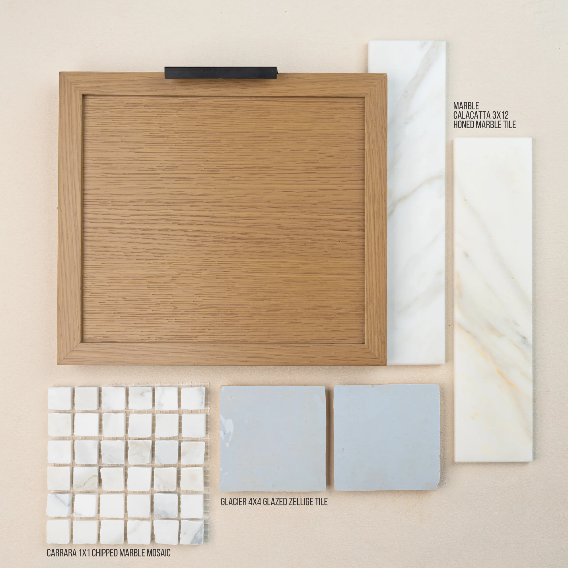 Flat lay of oak cabinet door with black handle, marble tile samples, glazed zellige tile, and chipped marble mosaic tiles