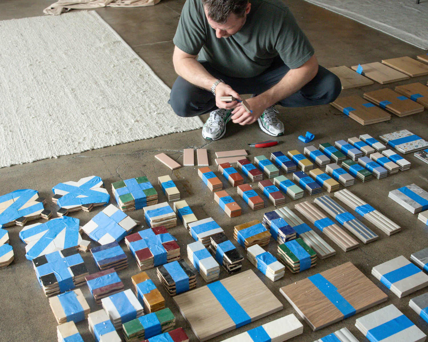 Man seated on floor carefully inspecting an extensive assortment of wooden and ceramic tile samples arranged in rows