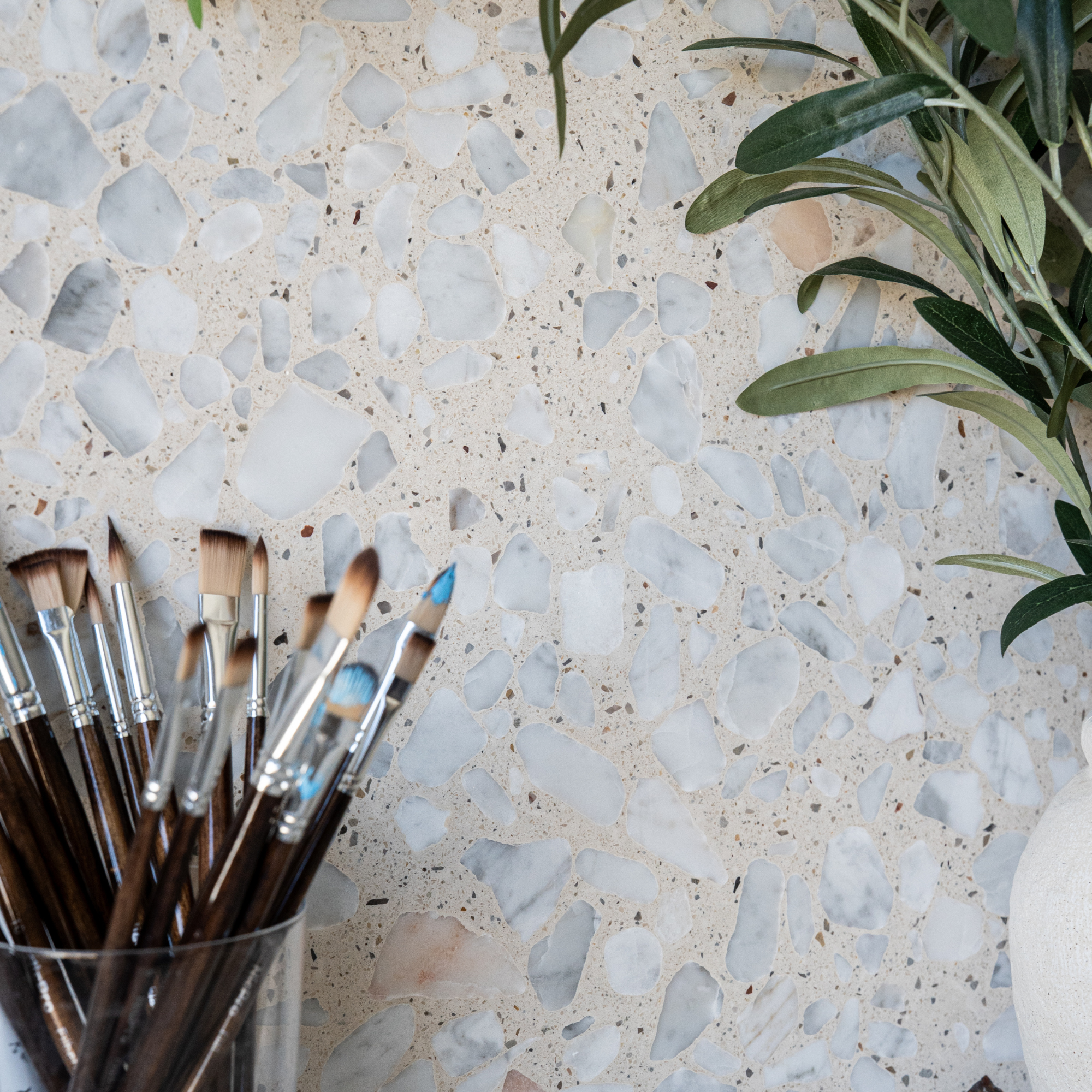 Terrazzo surface with pale stone chips beside paintbrushes and a leafy plant