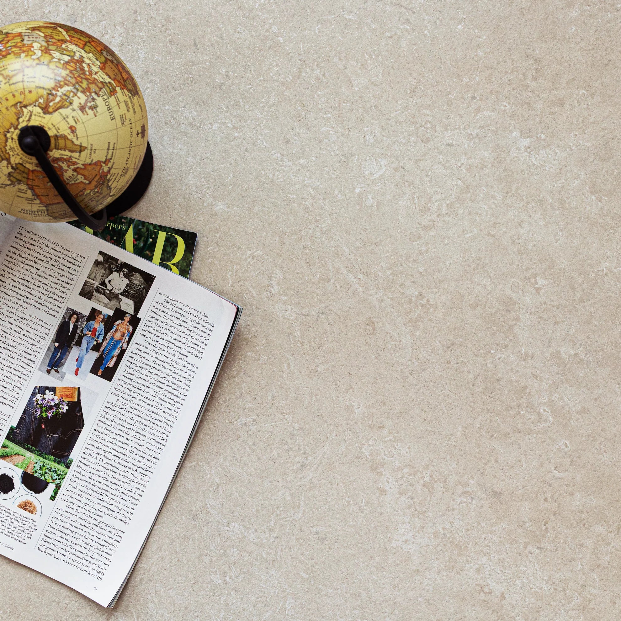 Beige large format tile surface with subtle texture, featuring an open magazine and a small vintage globe on the side
