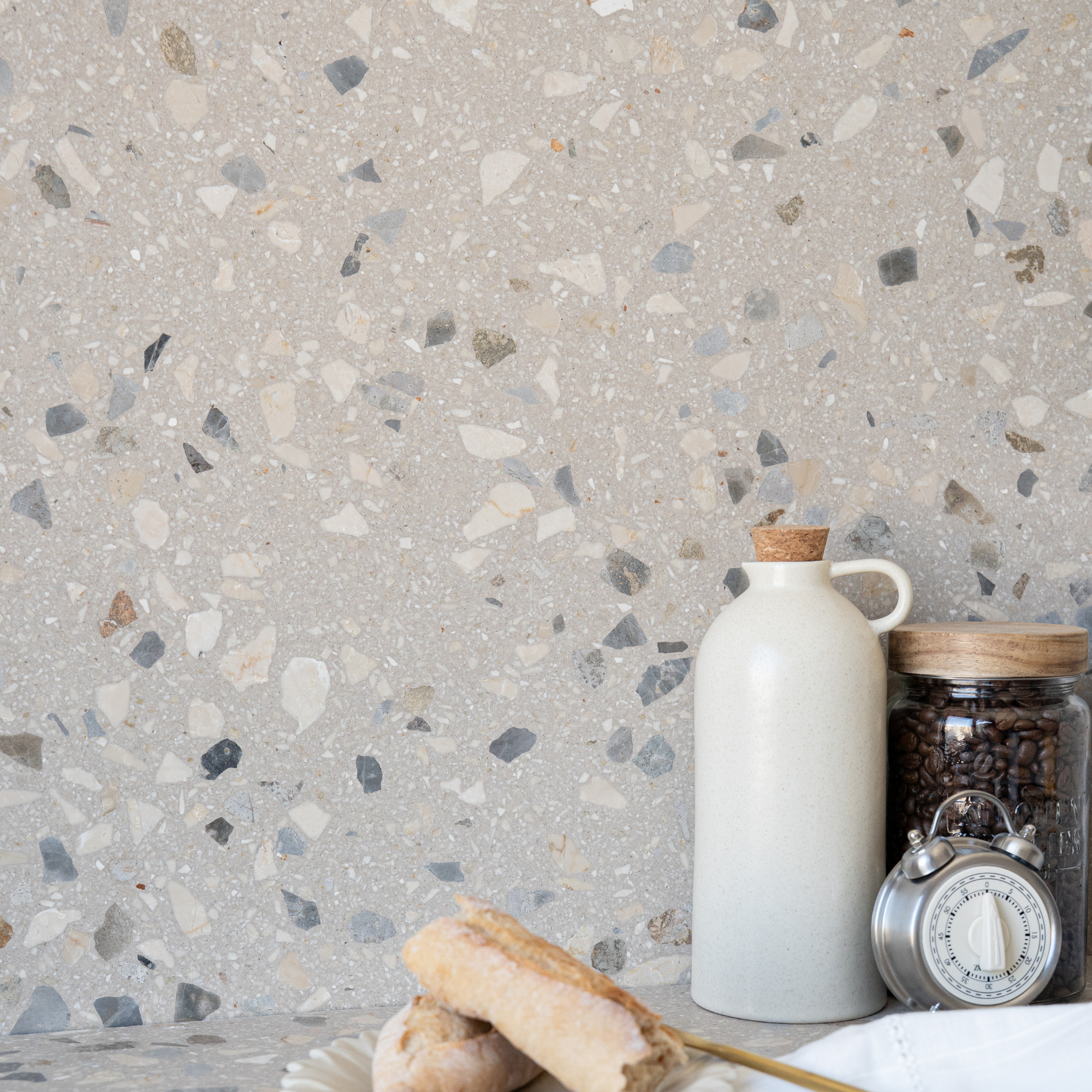 Speckled gray terrazzo wall and counter styled with a ceramic jug coffee jar alarm clock and pastries