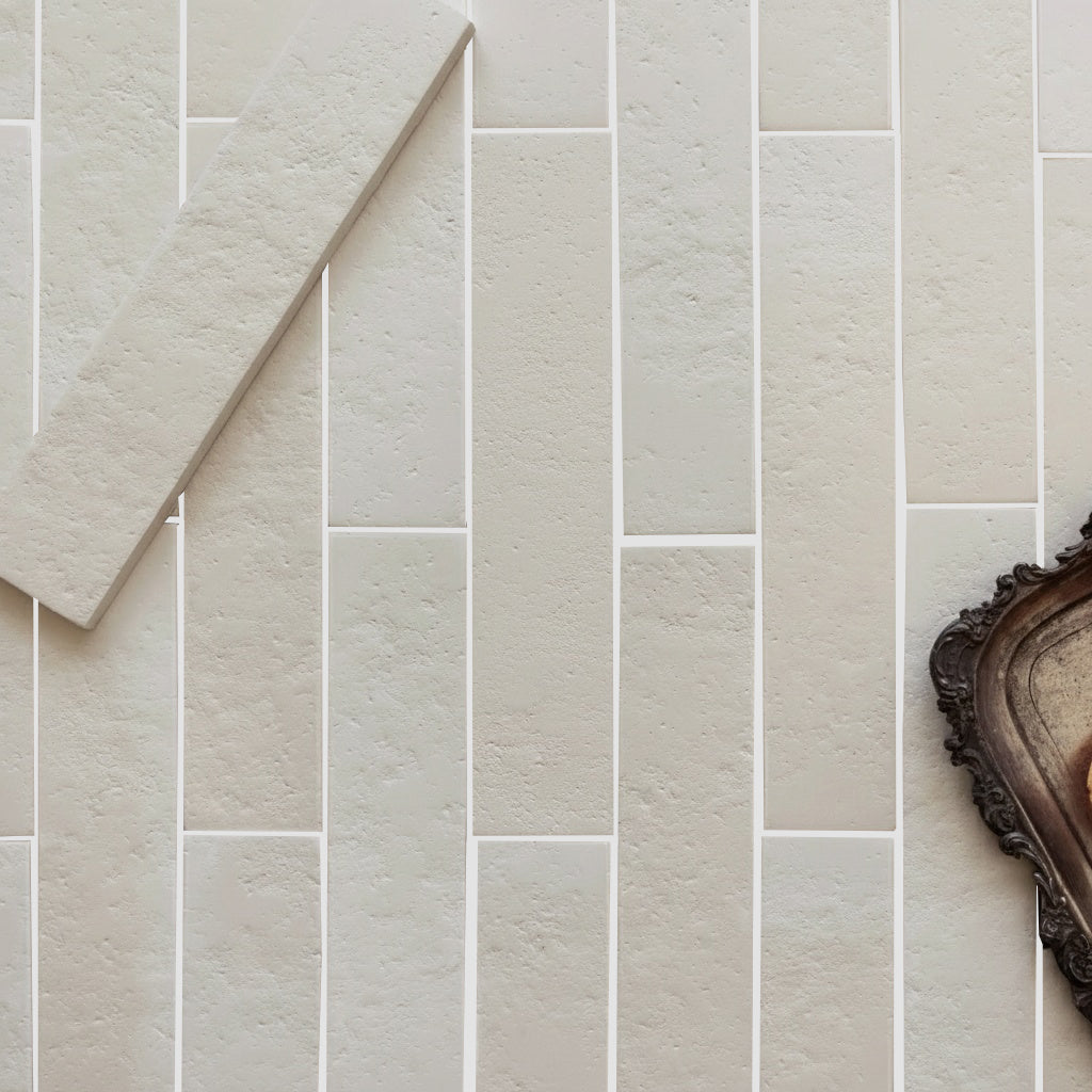 Rectangular light beige ceramic tiles with subtle texture arranged in a staggered pattern with vintage tray corner visible