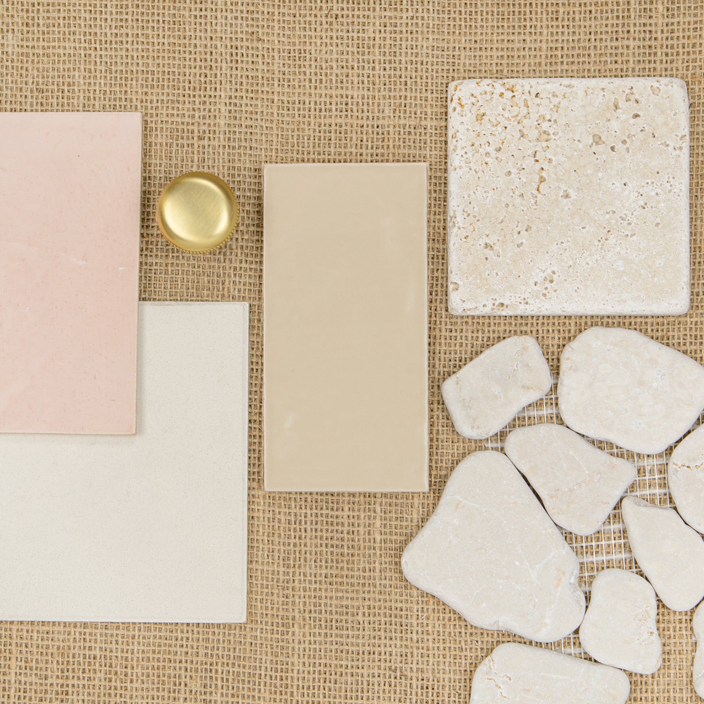 Assortment of ceramic and stone tiles in soft neutral tones arranged on textured burlap surface