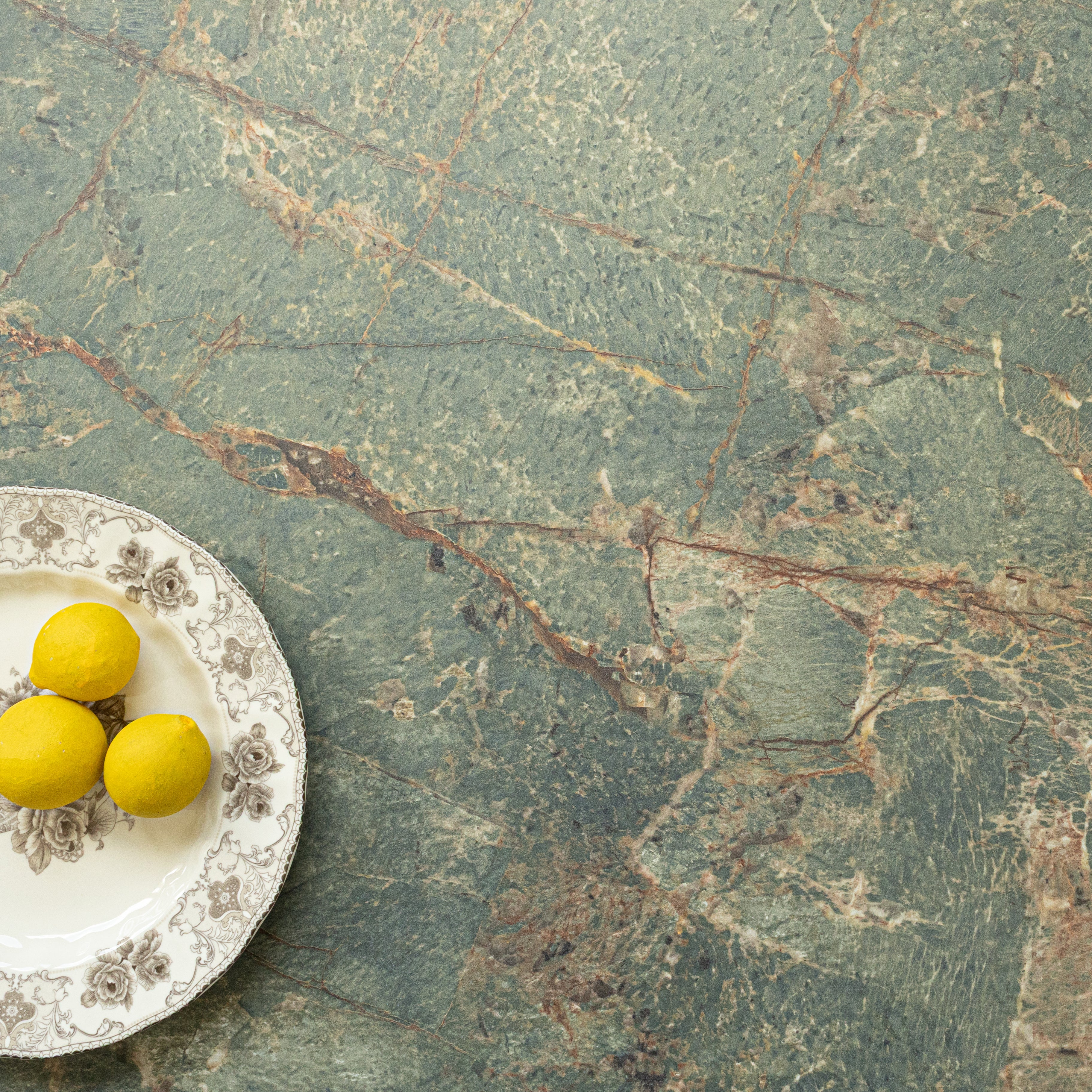 Green marble-inspired porcelain tile surface with natural veining and a decorative plate holding three lemons