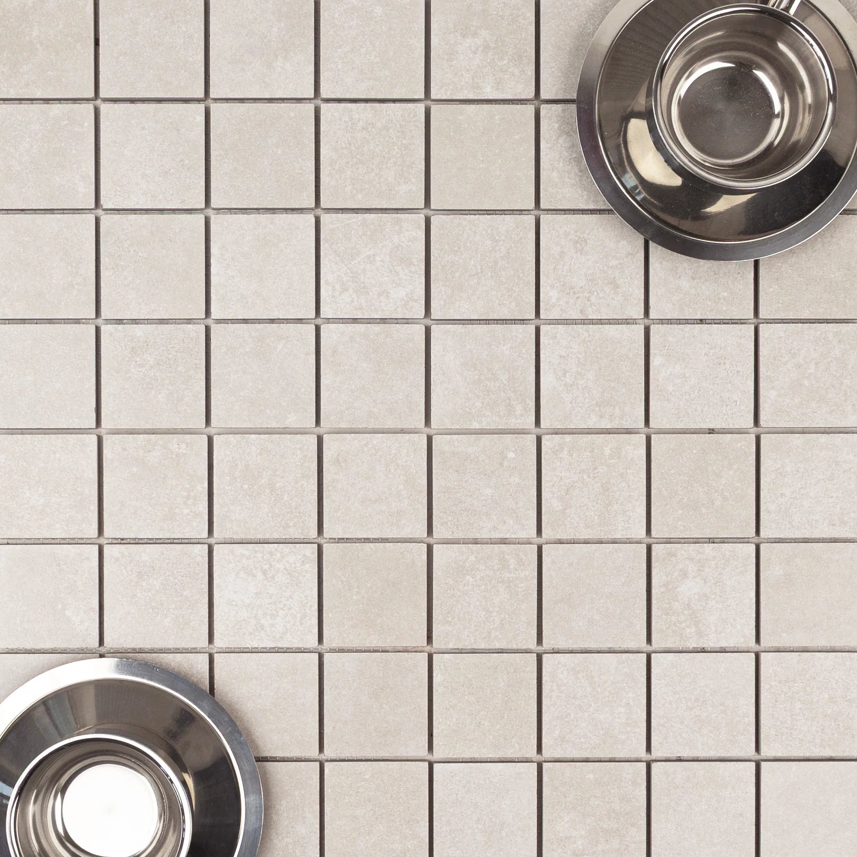 Light beige small-format porcelain tiles with a matte cement-like texture and two stainless steel bowls placed on top