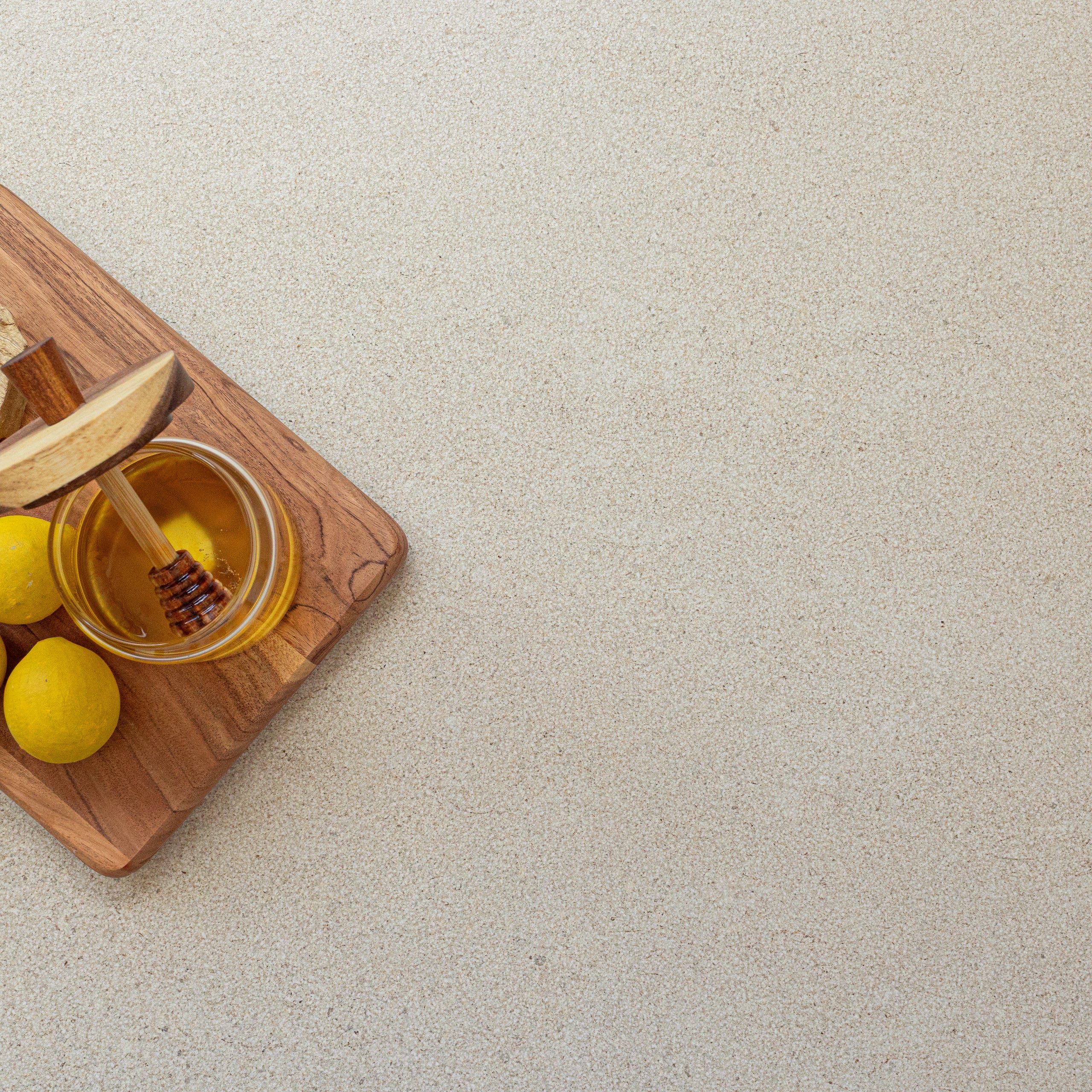 Light beige porcelain tile surface with fine natural texture and wooden board with honey jar and lemons in corner