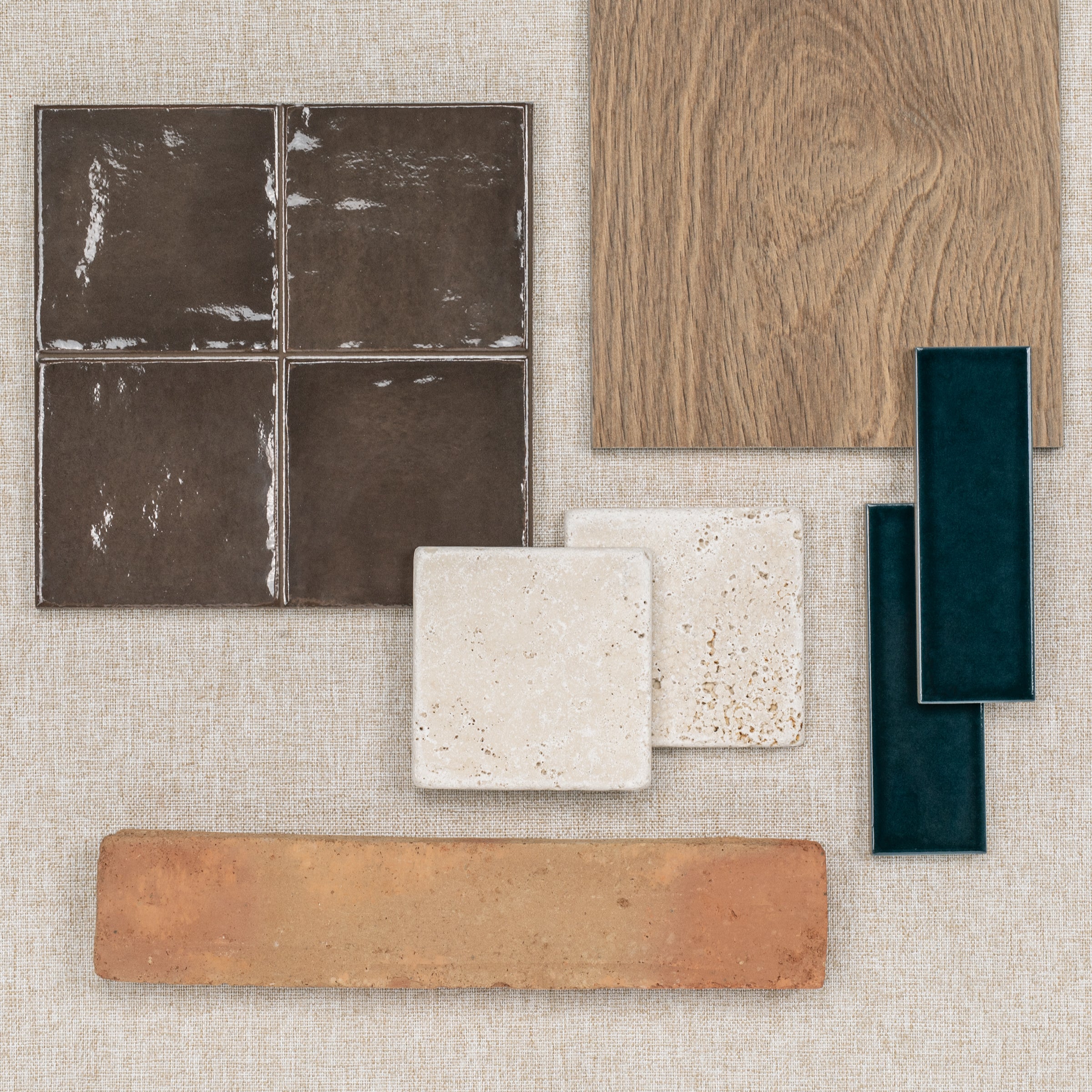 Assorted ceramic, porcelain, terracotta tiles, wood plank, and textured tile samples on neutral fabric background