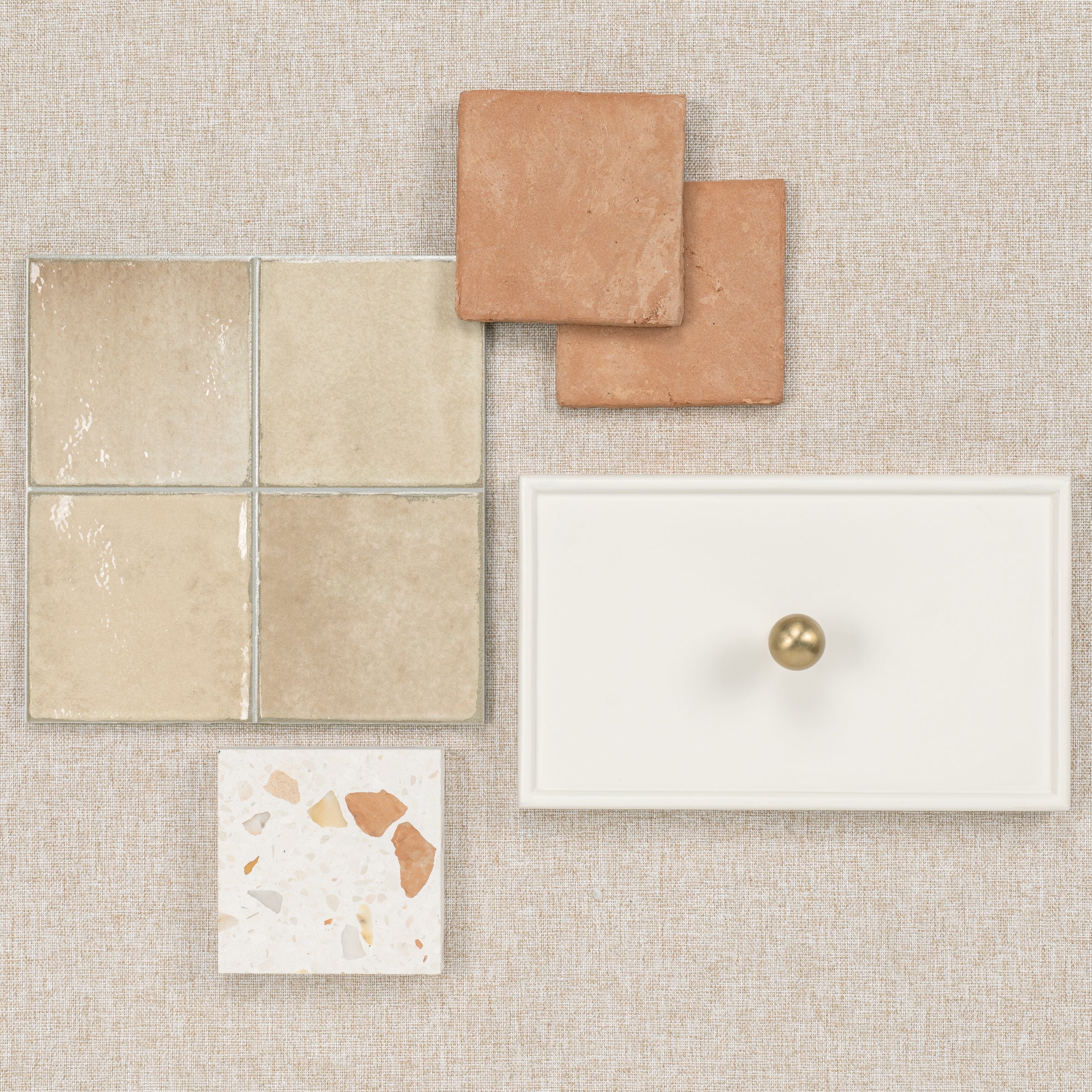 Beige, terracotta, and terrazzo tiles with a white drawer front featuring a round brass knob on a textured background