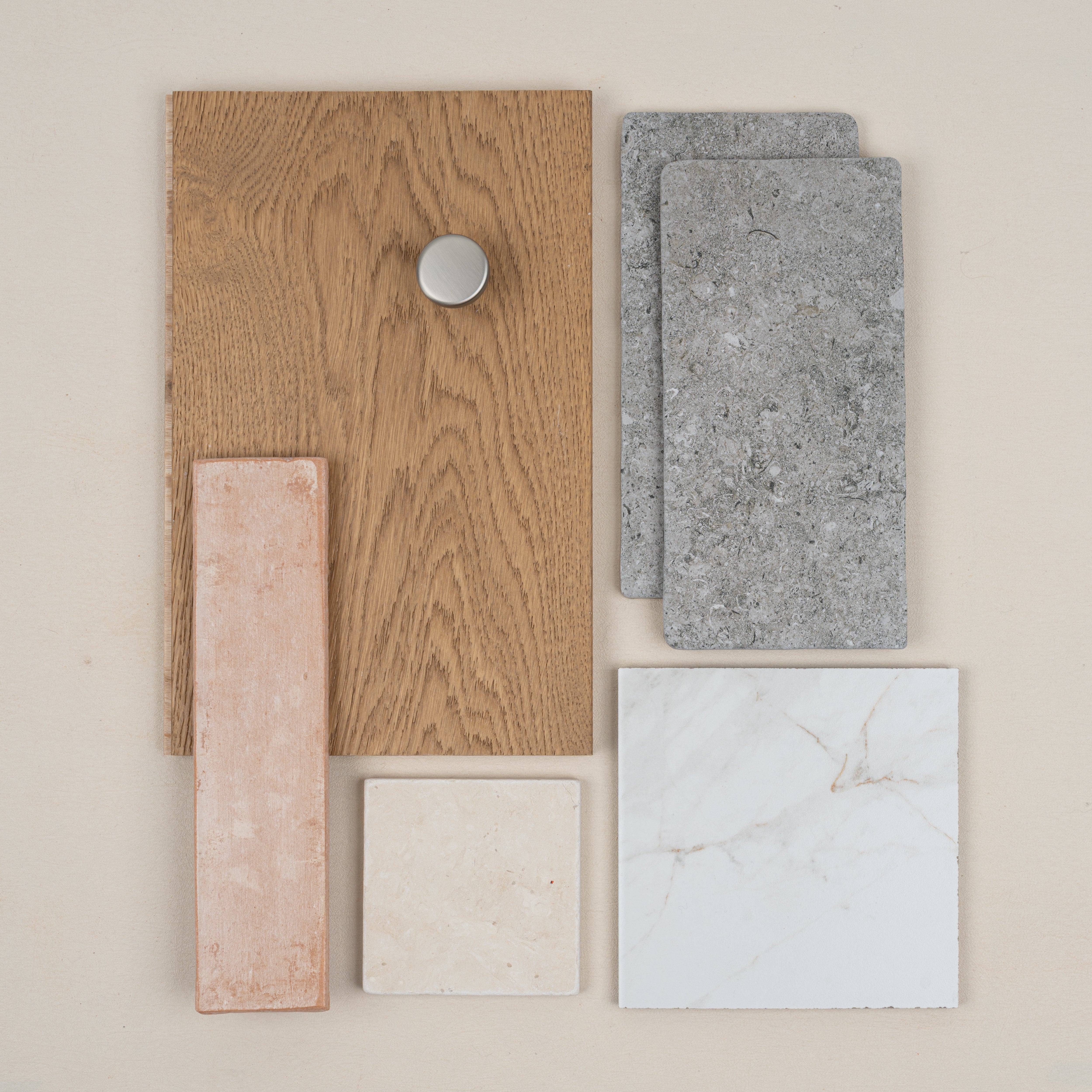 Arrangement of light oak wood with silver knob, textured gray stone tiles, beige ceramic, white marble, and terracotta tile samples
