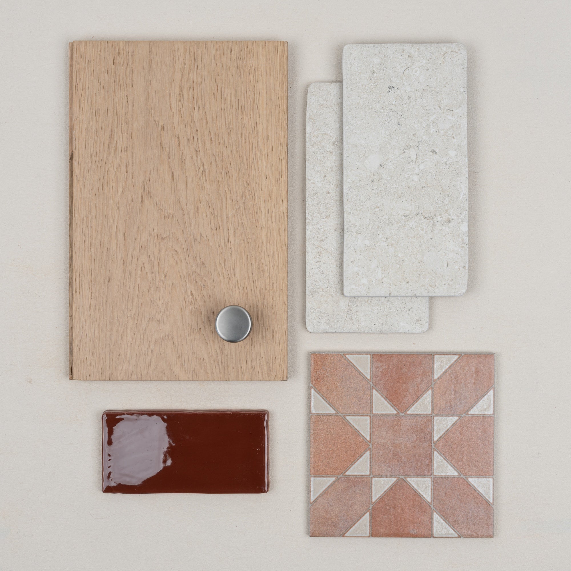 Flat lay of light oak wood sample with silver knob, textured white stone tiles, glossy deep red tile, and patterned terracotta ceramic tile