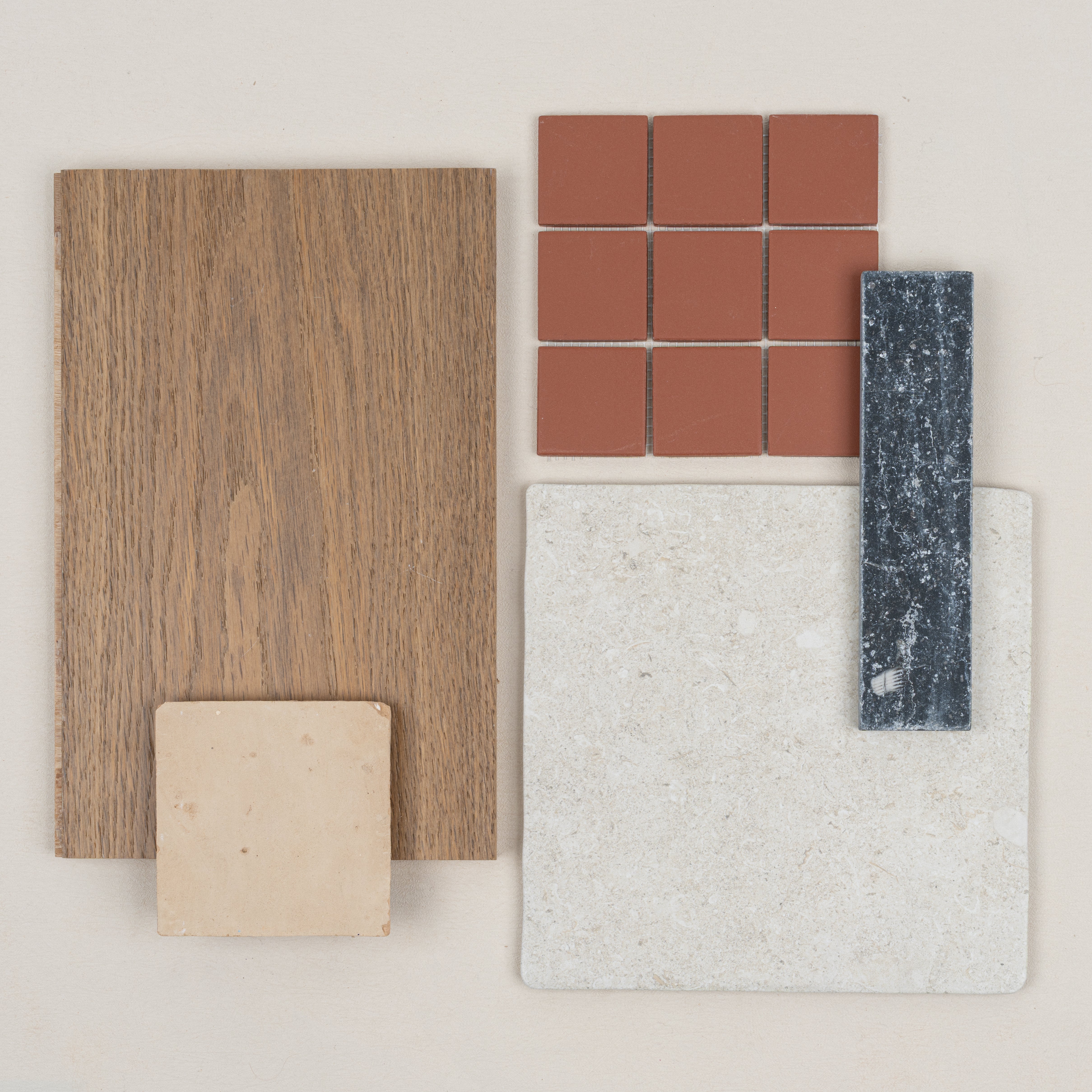 Natural wood sample alongside terracotta tiles, cream ceramic, and dark textured stone tile on pale background