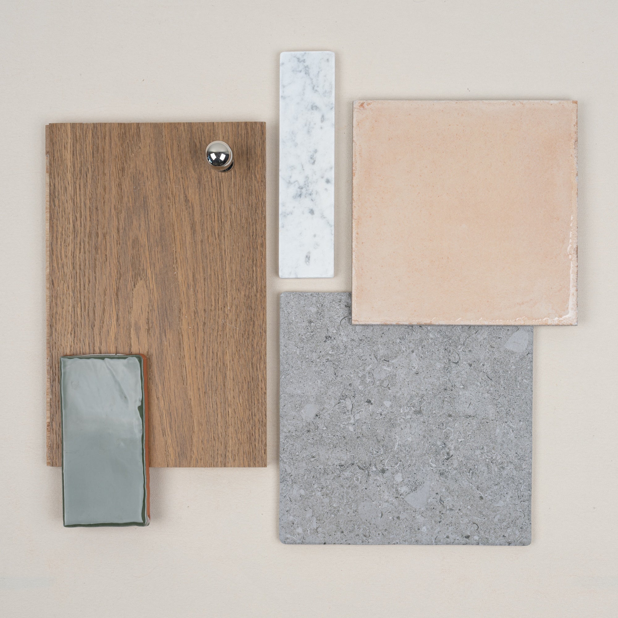 Flat lay of oak wood sample with silver knob, beige ceramic tile, gray stone tile, narrow white marble, and glossy gray ceramic tile