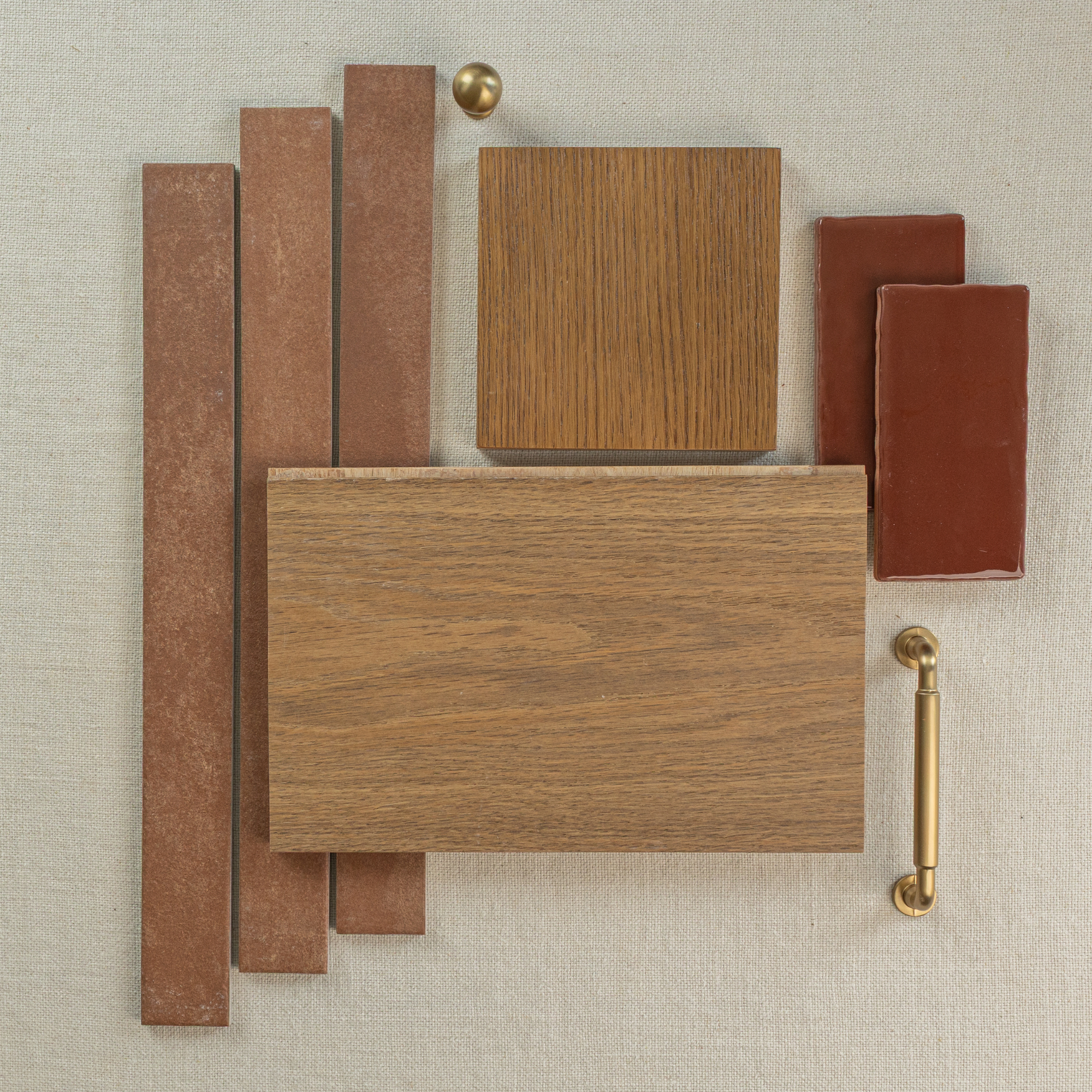 Flat lay of warm terracotta tiles, oak wood samples, and brass hardware on a neutral fabric background