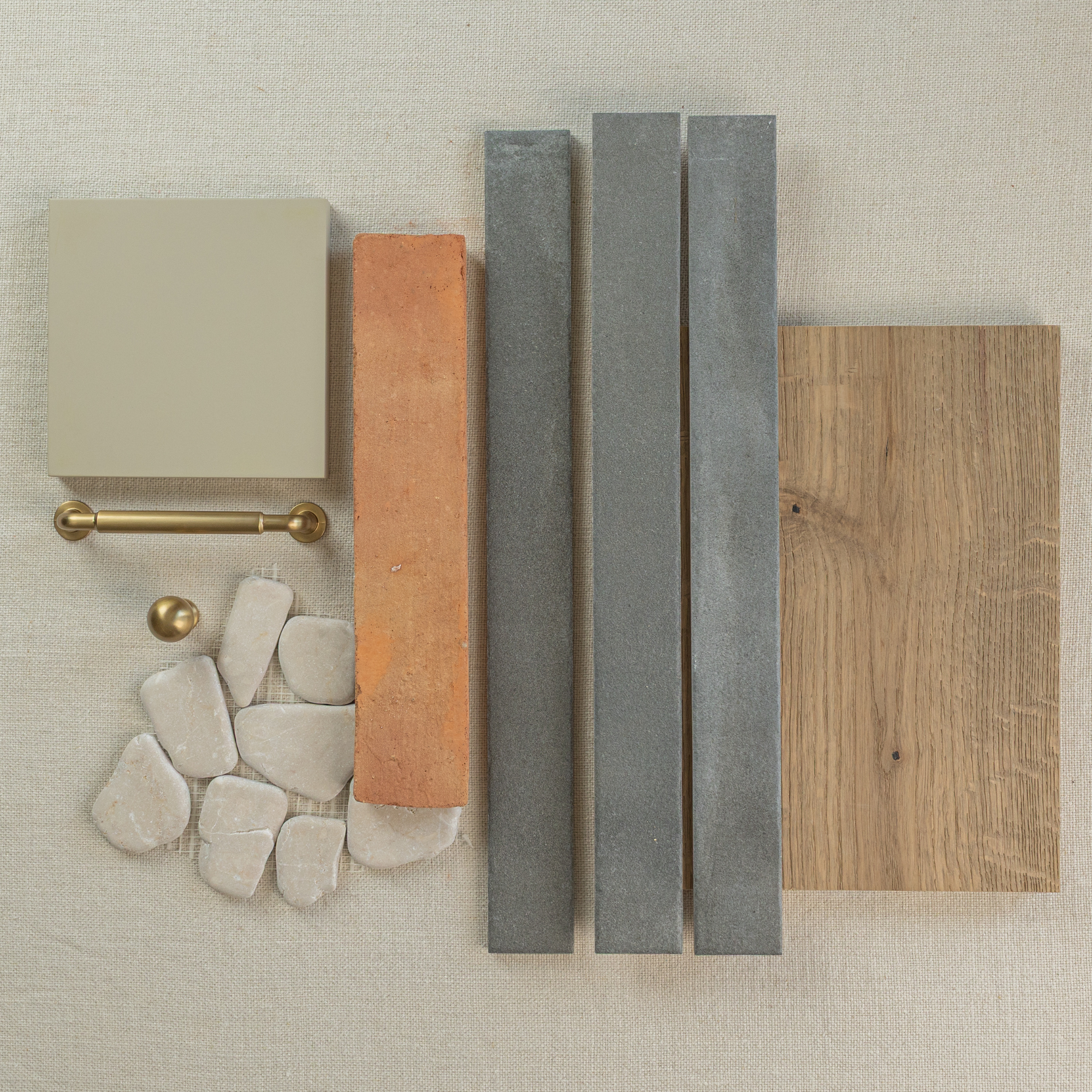 Arrangement of beige, terracotta, gray slim tiles, natural stones, brass hardware, and oak wood sample on fabric surface
