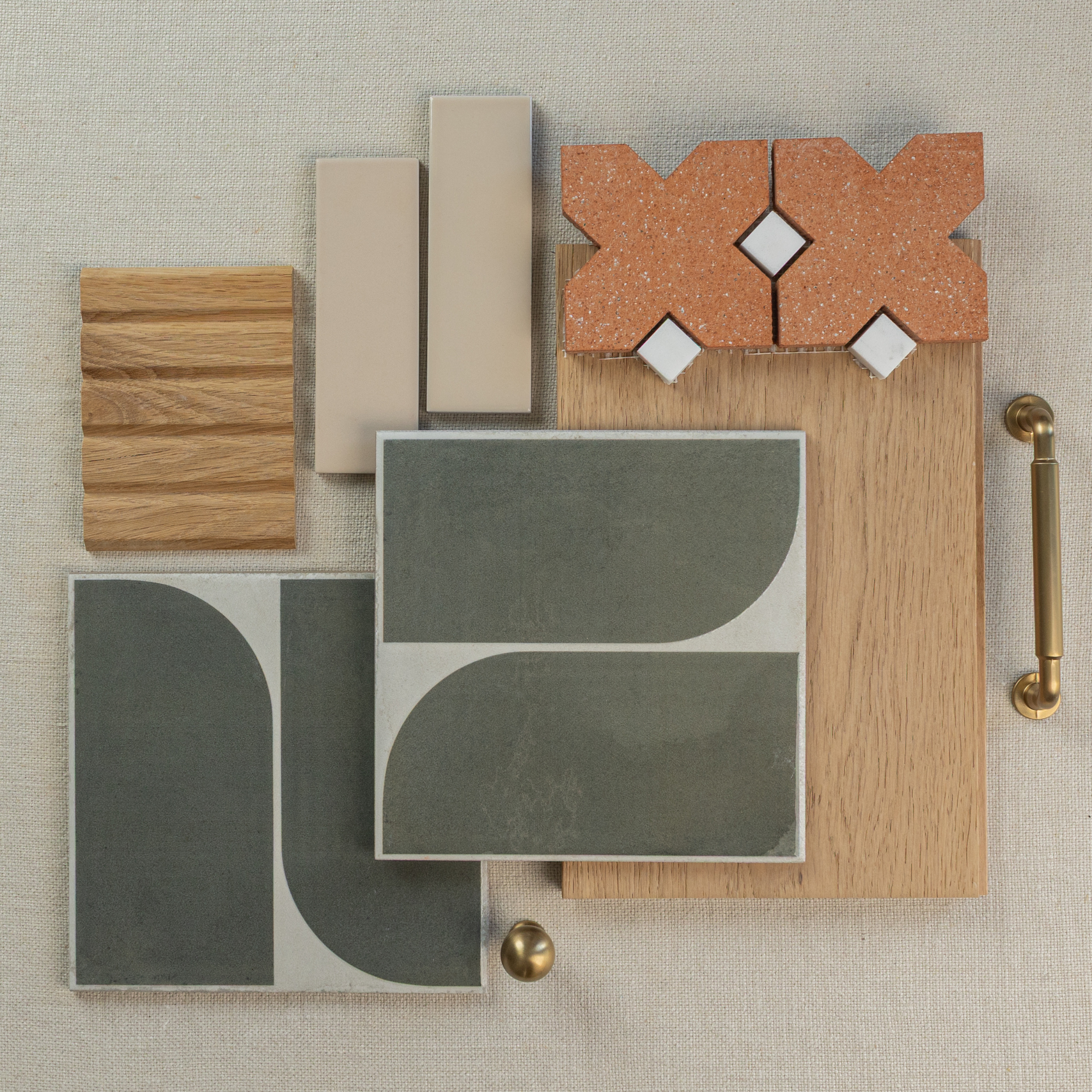 Flat layout of green ceramic patterned tiles, terracotta cross-shaped tiles, light oak wood samples, beige ceramic tiles, and brass handles on fabric background