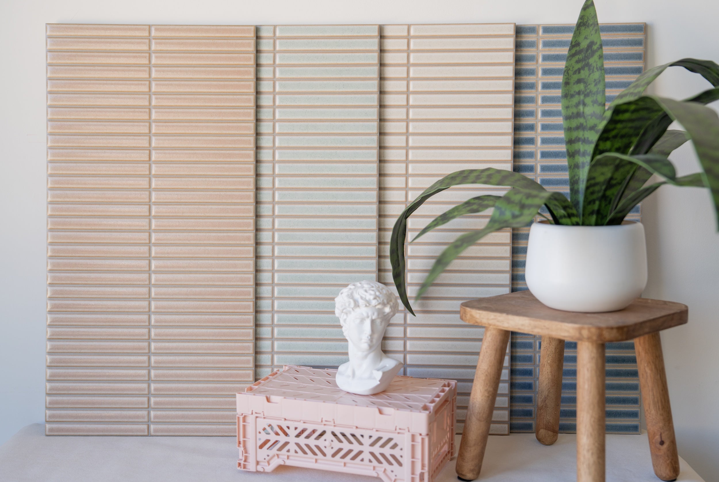 Vertical rectangular ceramic tiles in beige, light gray, and blue tones displayed with plant and sculptural bust accents