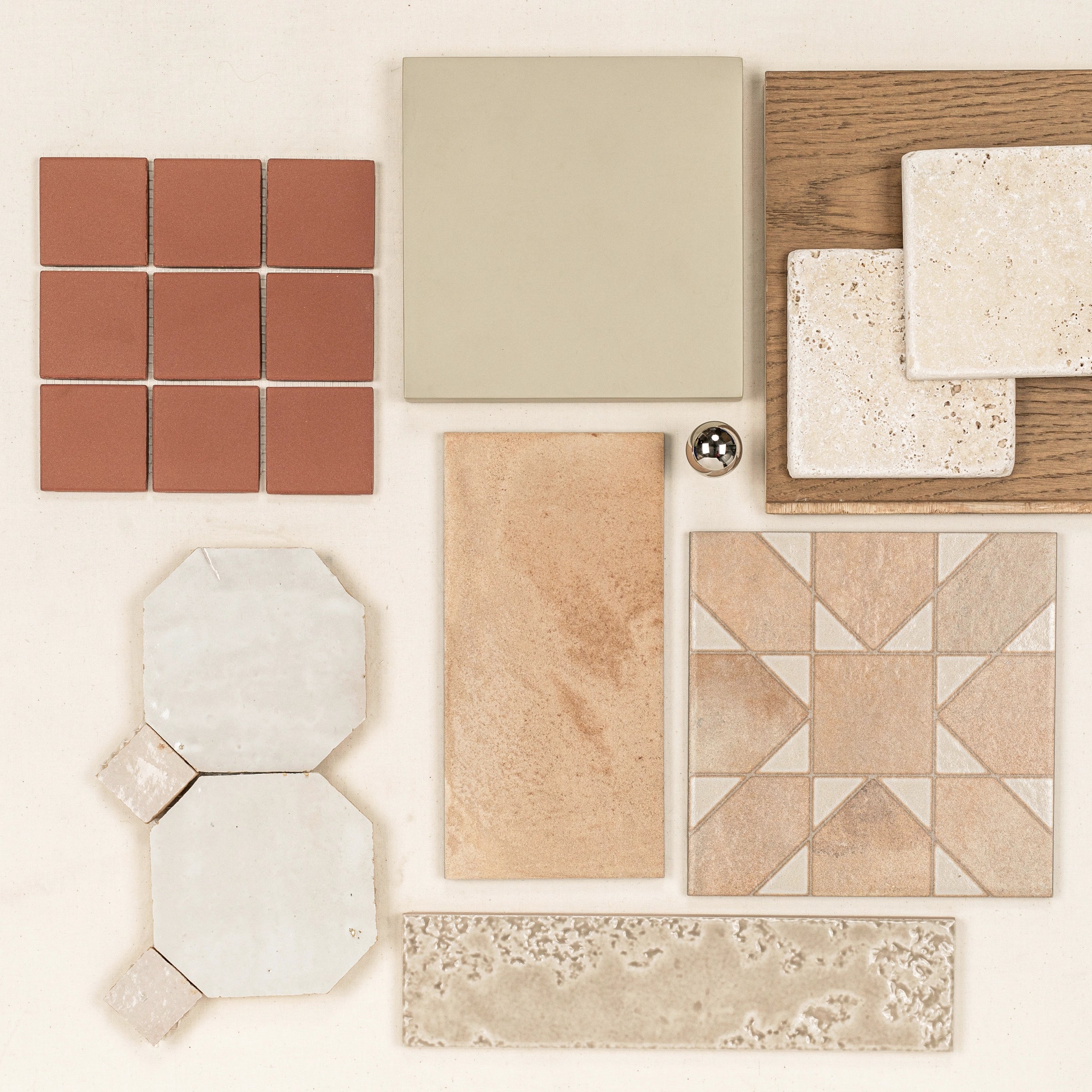Assortment of ceramic and porcelain tiles in natural tones, wood sample, and a metallic sphere arranged on a neutral surface