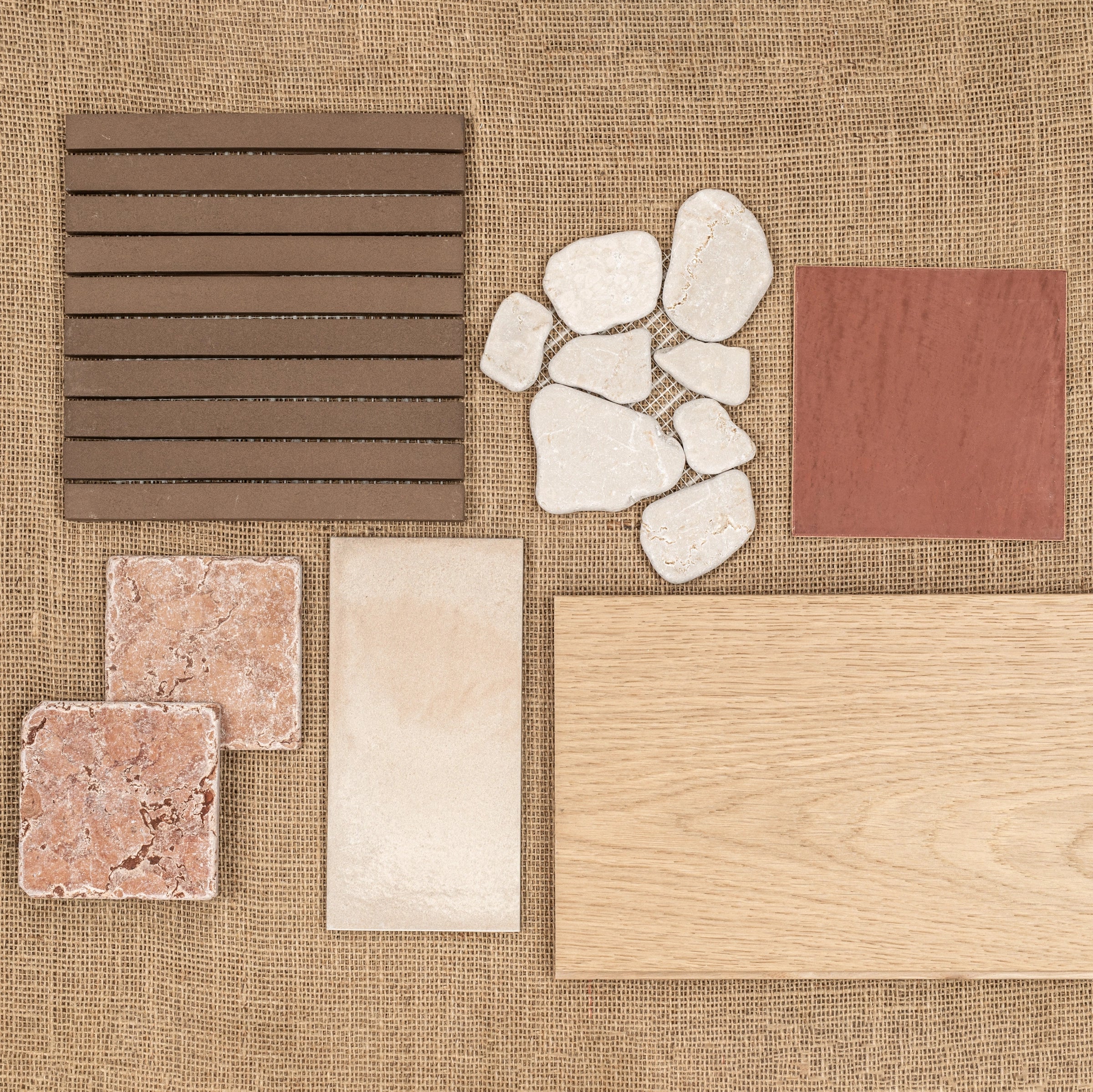 Arrangement of natural stone pieces, textured tiles, terracotta square, and wood sample on woven fabric background
