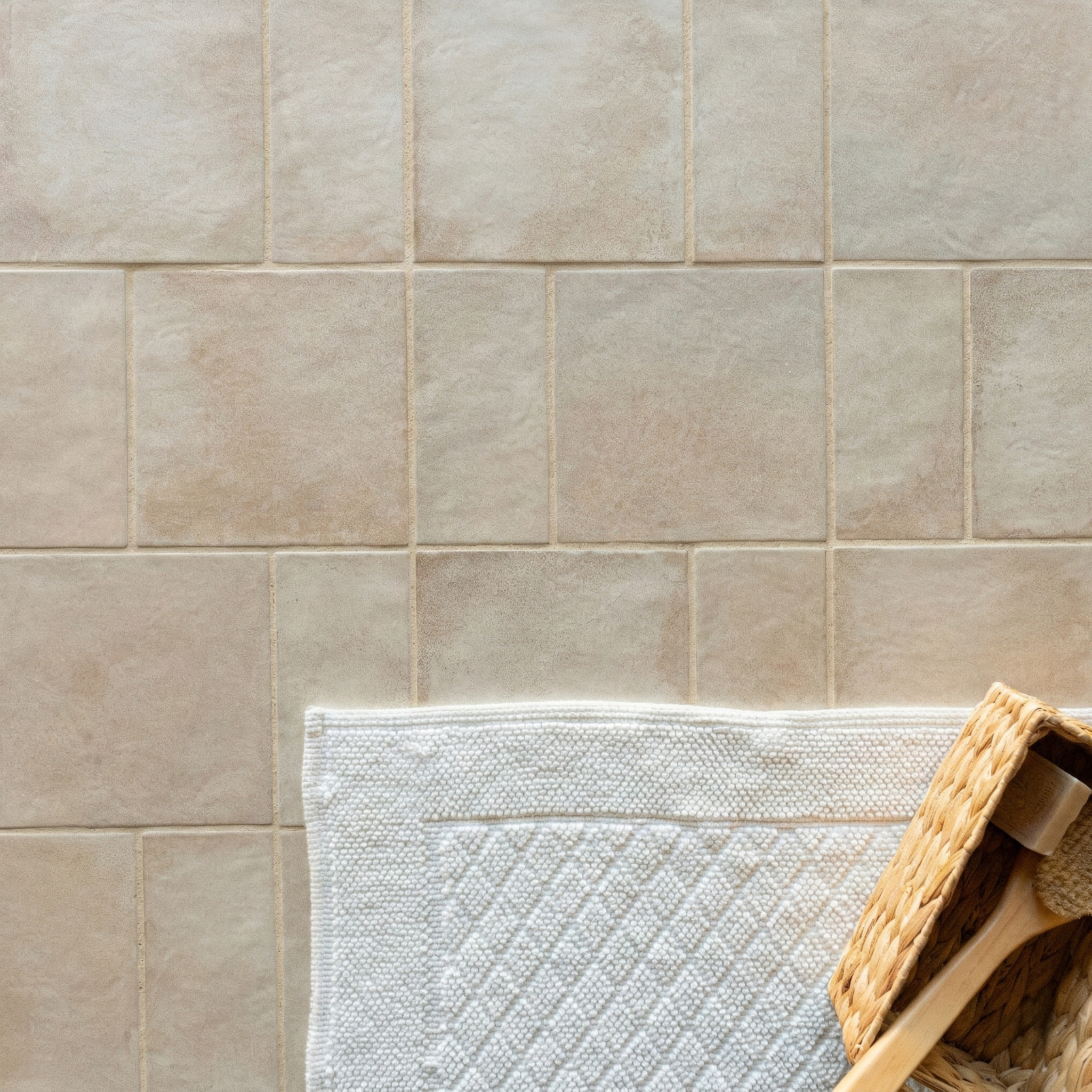 Square ceramic tiles in soft beige with natural texture paired with a woven white rug and wicker basket edge