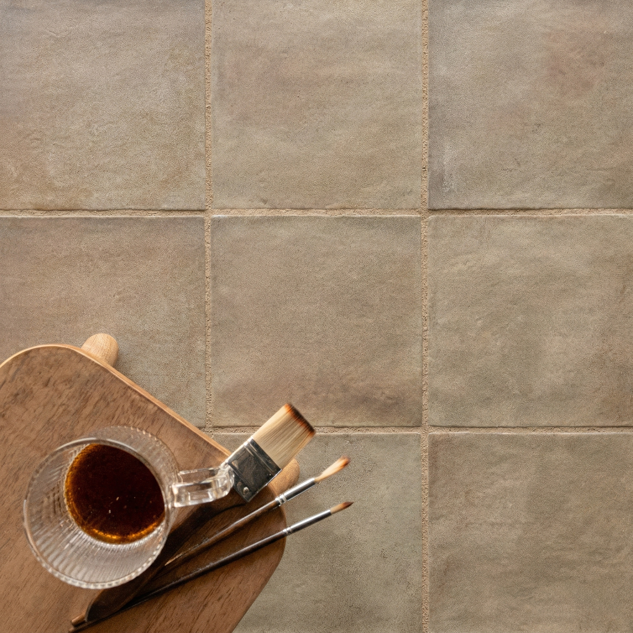 Square ceramic tiles in sandy beige with a matte, slightly textured surface and subtle color variations on a neutral background