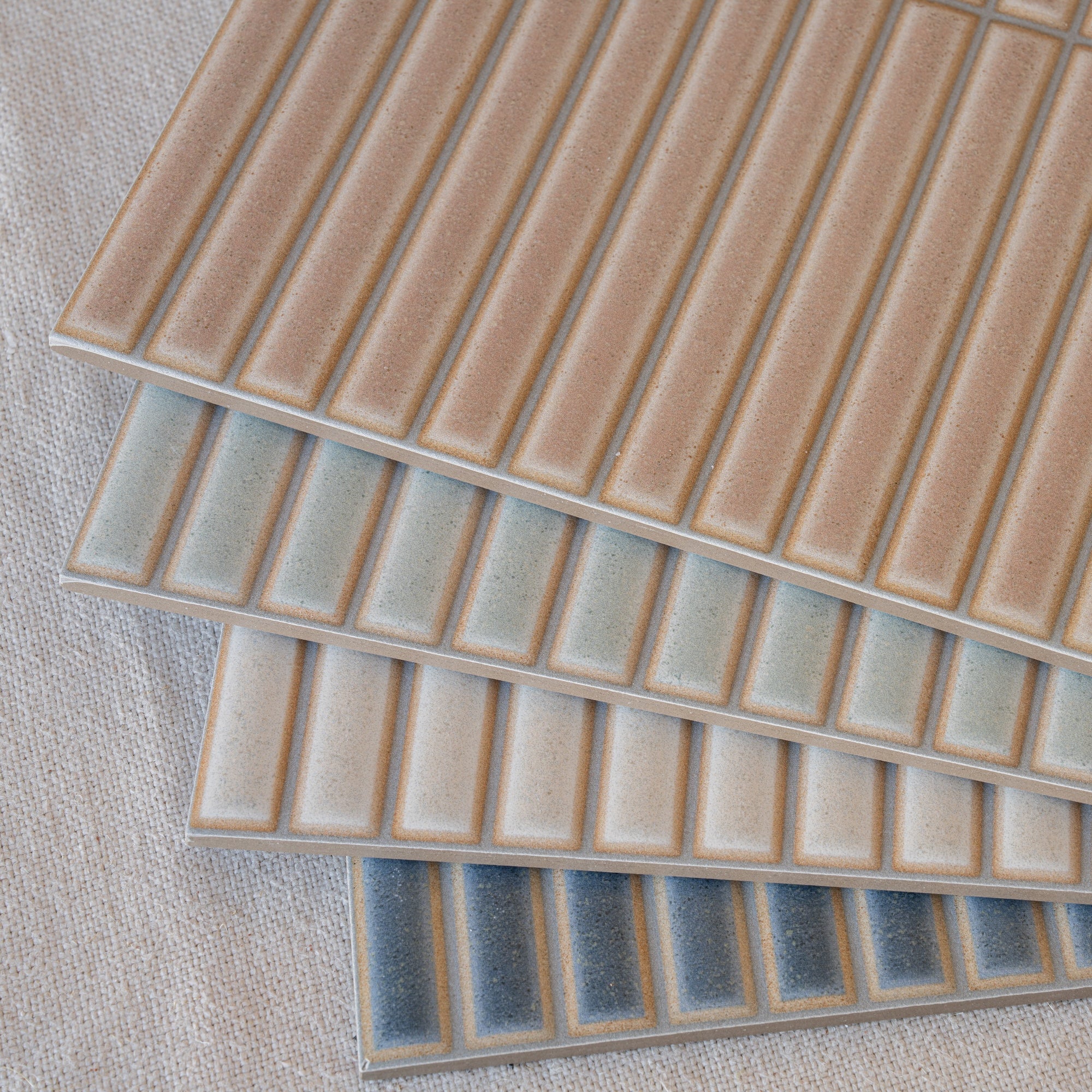 Three overlapping rectangular ceramic tile samples in warm beige and gray tones with a textured linear pattern