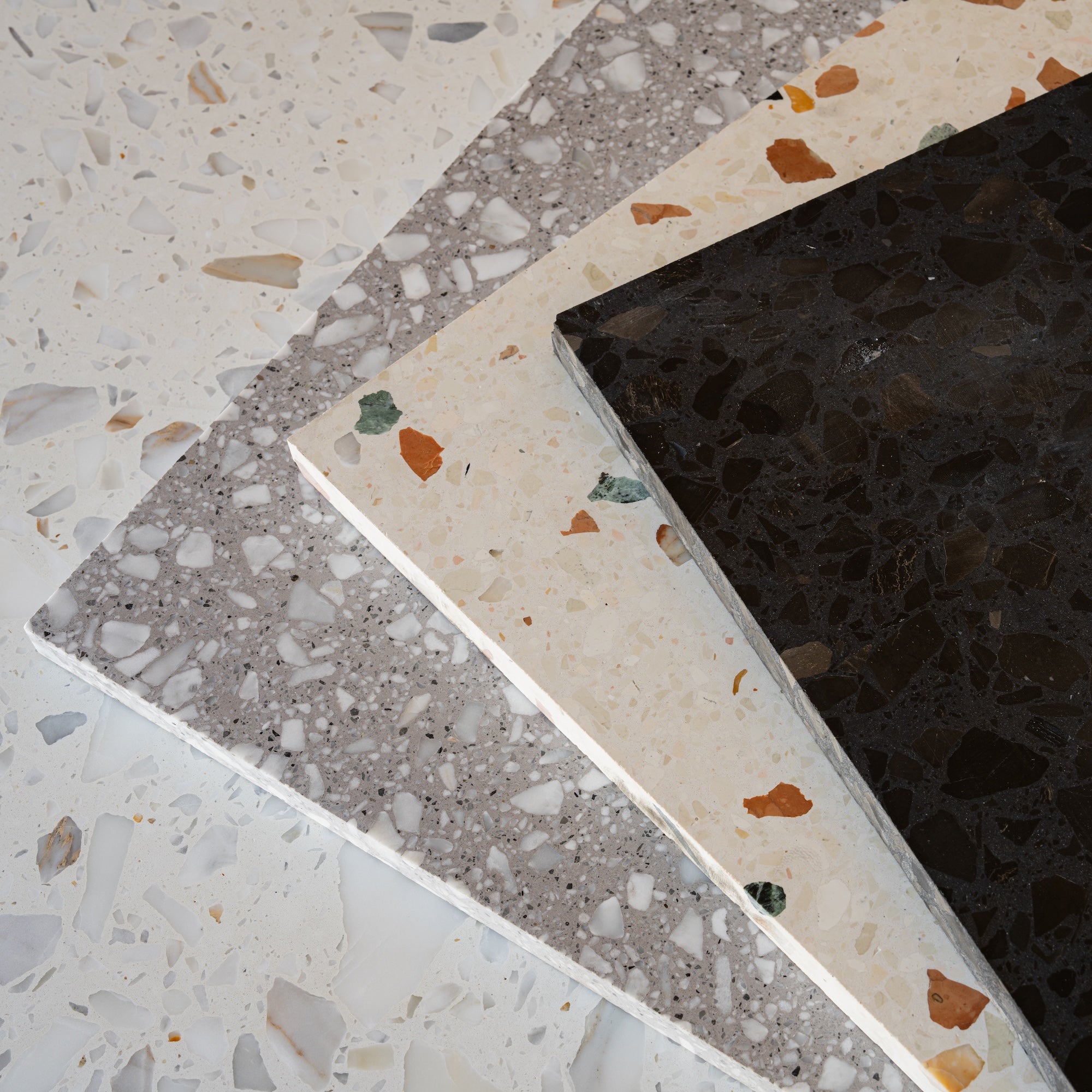 Four terrazzo tile samples in cream, gray, beige, and black tones showing varied aggregate patterns and textures