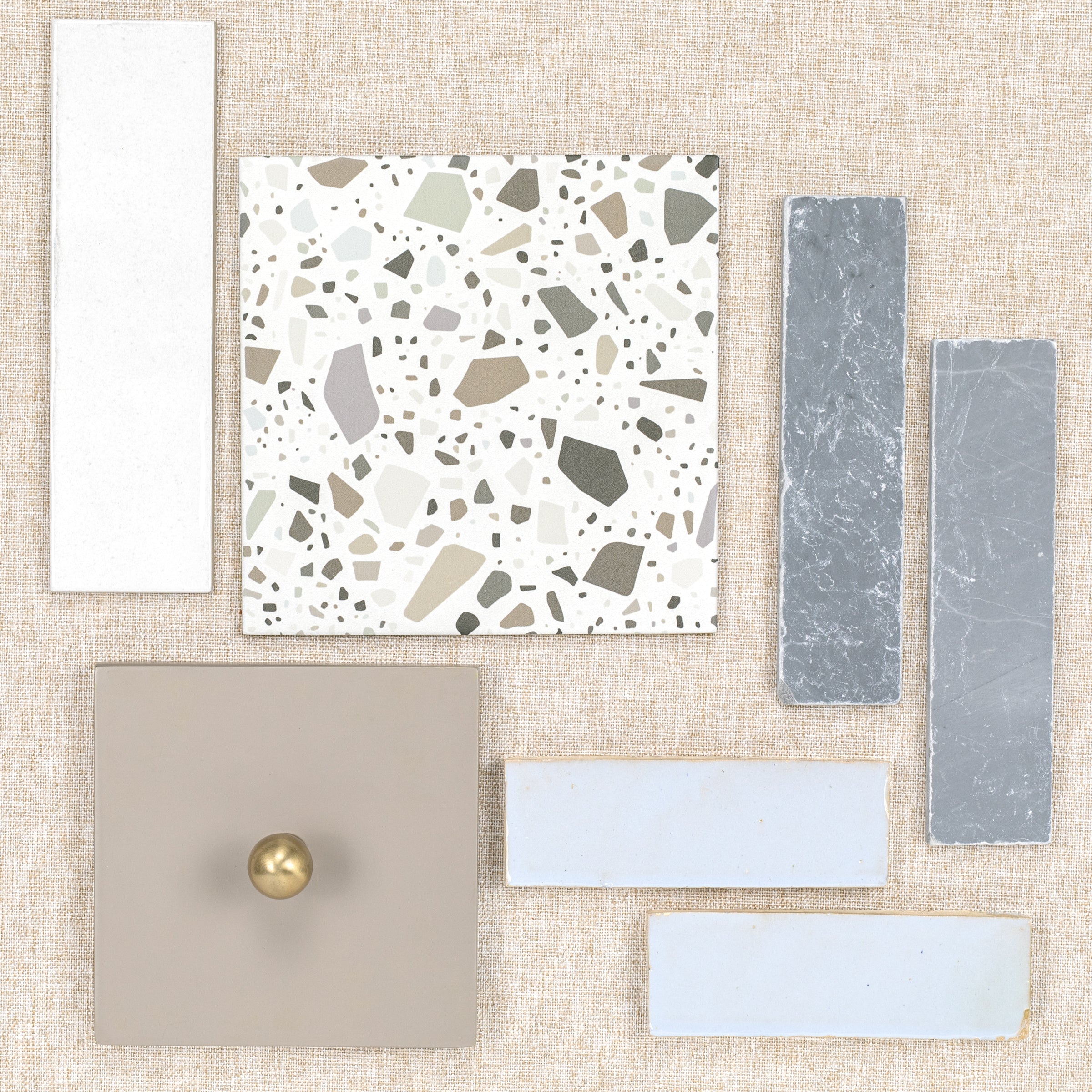 Flat lay of assorted ceramic and porcelain tile samples on textured beige background with a brass knob on one tile