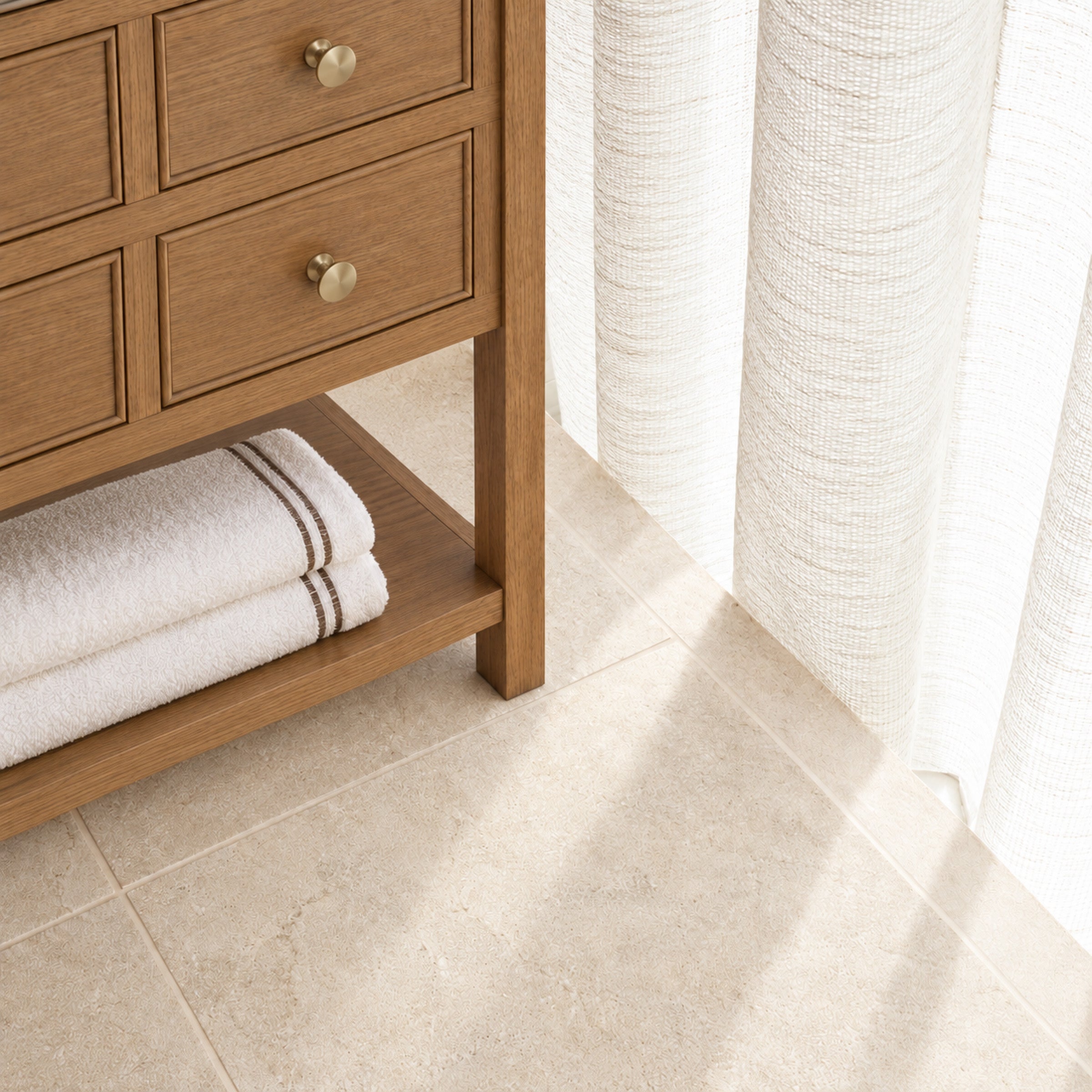 Wood bathroom vanity with folded towels over a beige tiled floor in sunlight