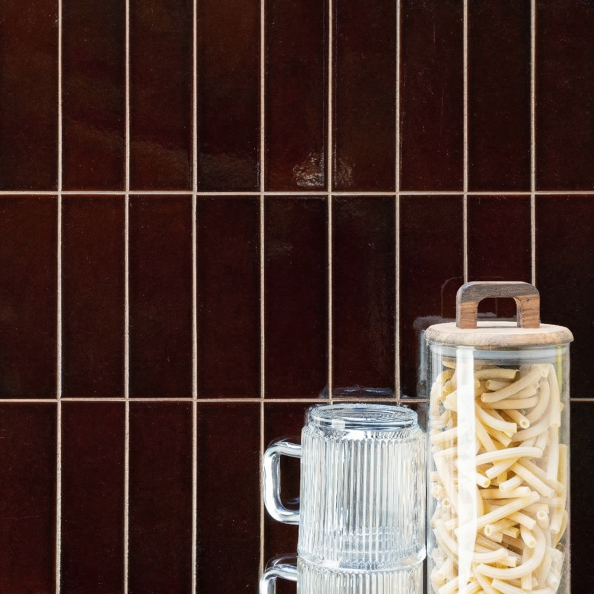 Glossy mahogany ceramic tiles in a vertical grid pattern with clear ribbed glass and a jar of dried pasta alongside