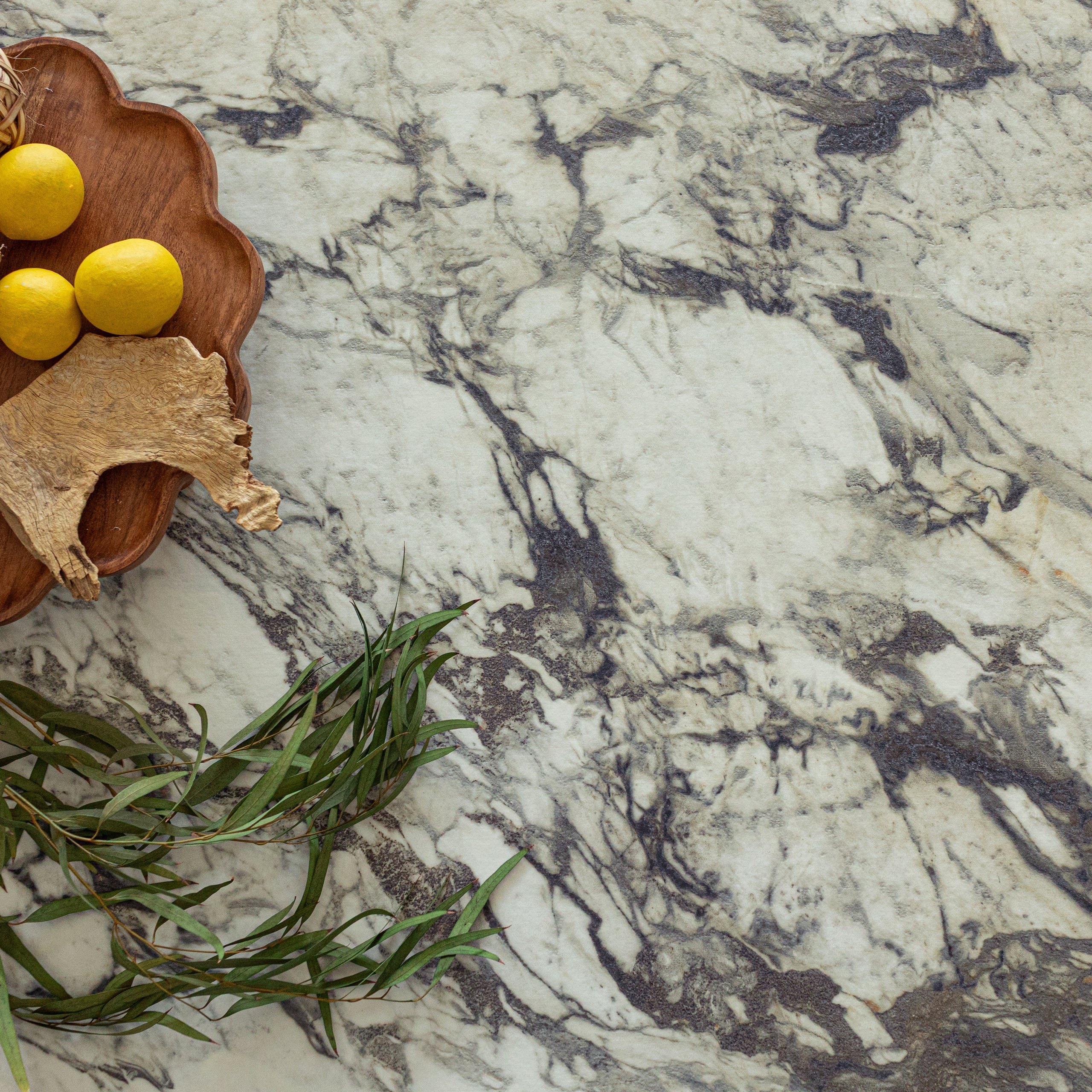 Light marble-look porcelain tile surface with dark veining, accented by a wooden tray holding lemons and green foliage nearby