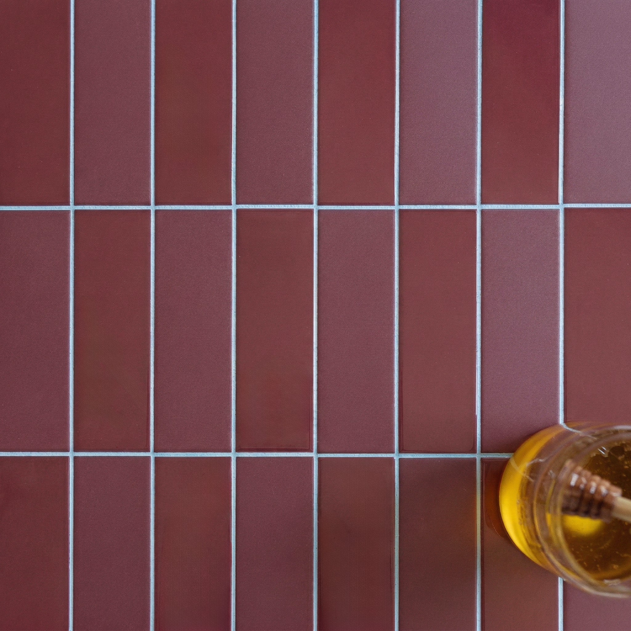 Close-up of vertical rectangular burgundy porcelain tiles with white grout and a honey jar on the side on tile surface