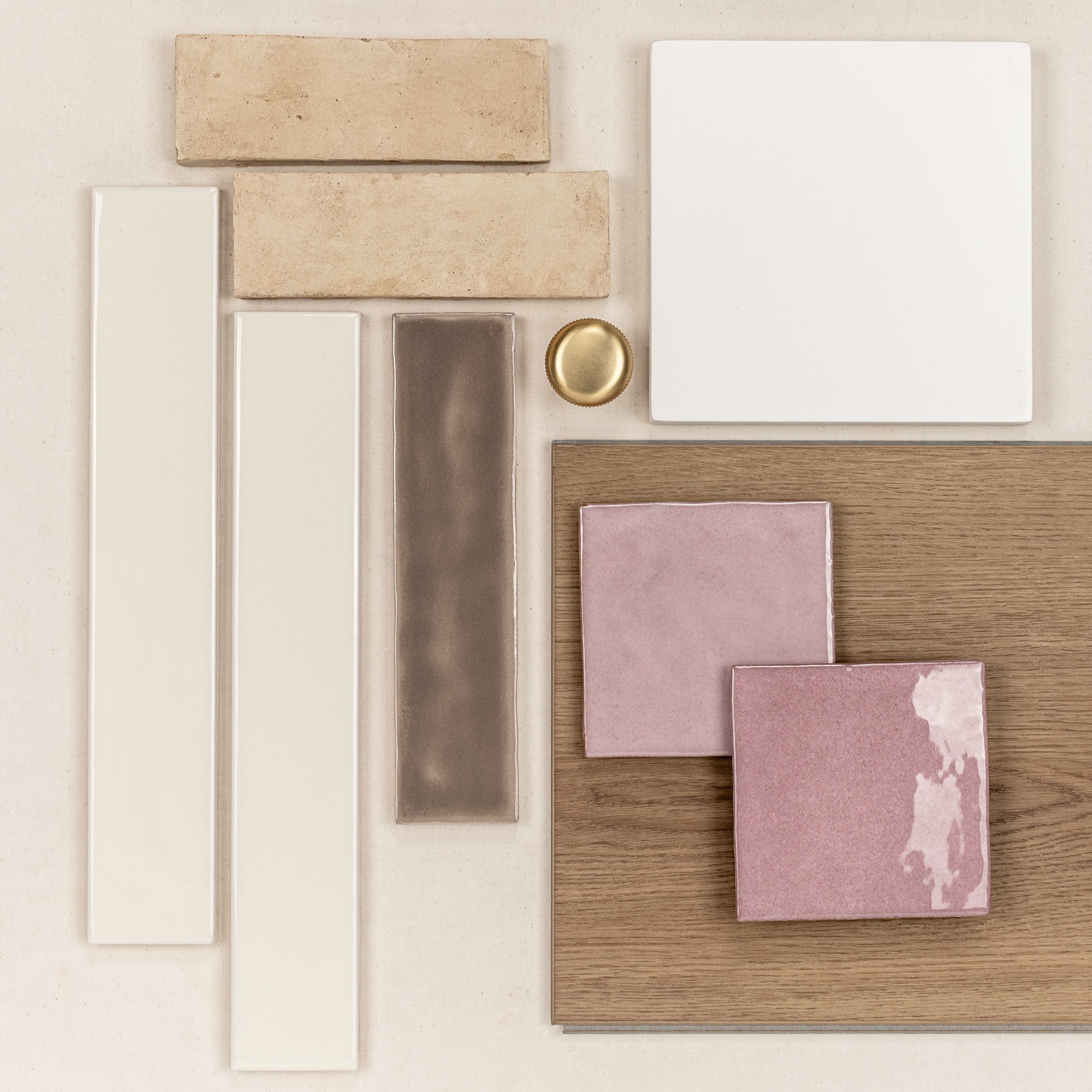 Glossy pink and matte beige ceramic tiles arranged on wood and neutral backgrounds with a polished brass round knob nearby