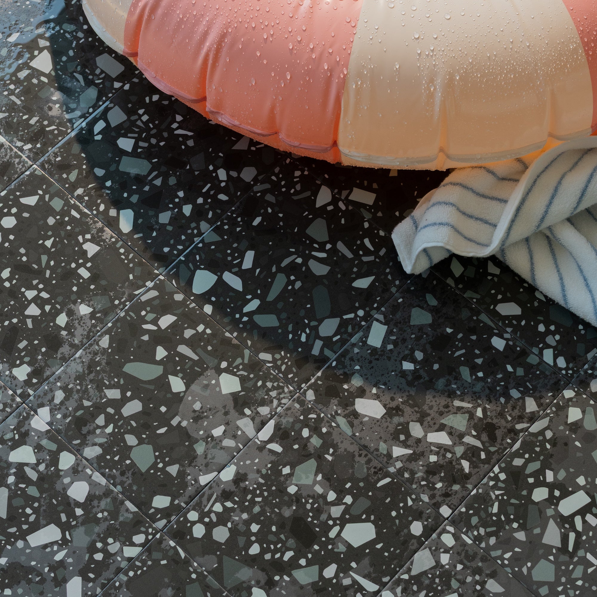 Black terrazzo tiles with white and gray flecks under a pink inflatable ring and striped towel.