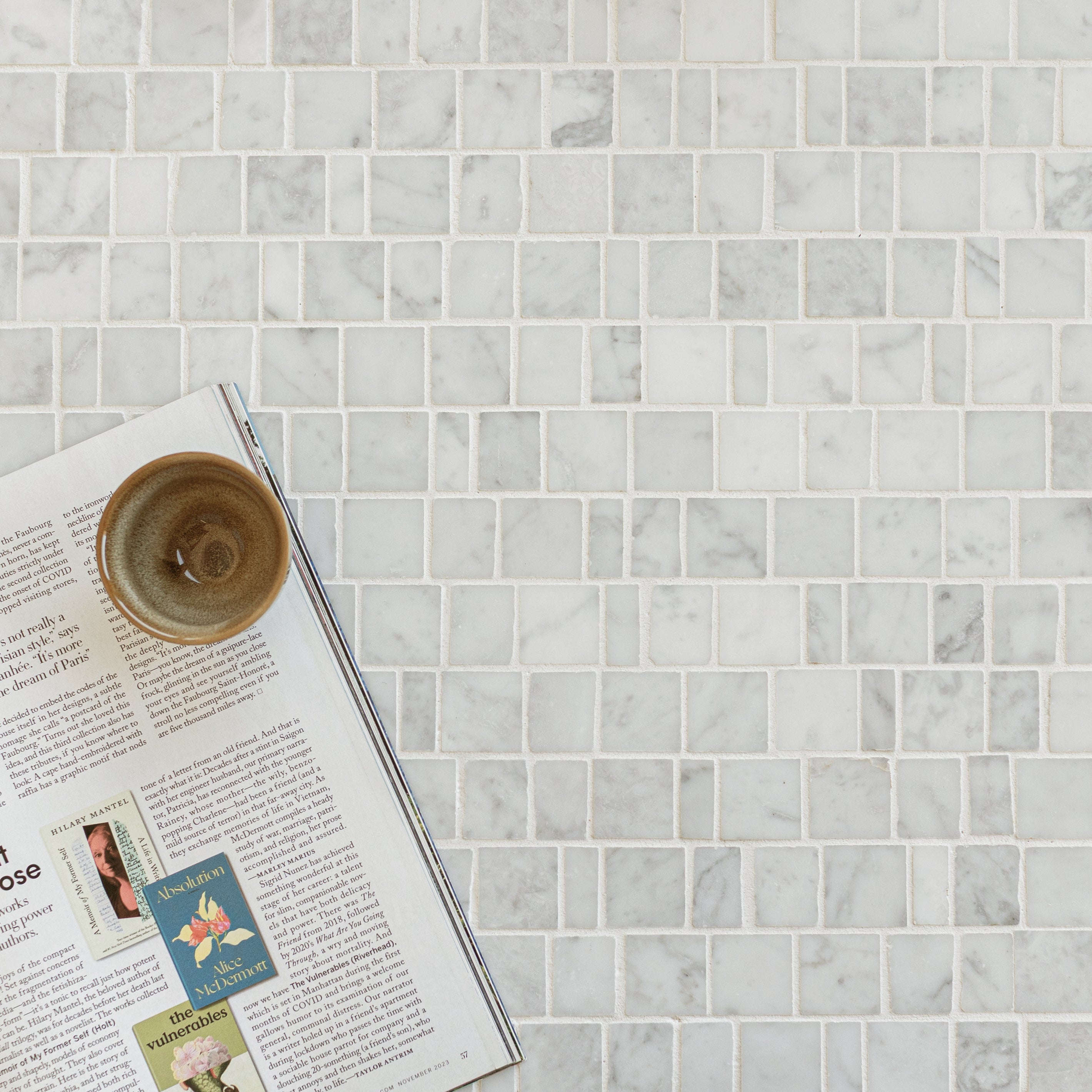 Light gray and white marble mosaic tiles arranged in a running bond pattern with a ceramic cup and open magazine nearby