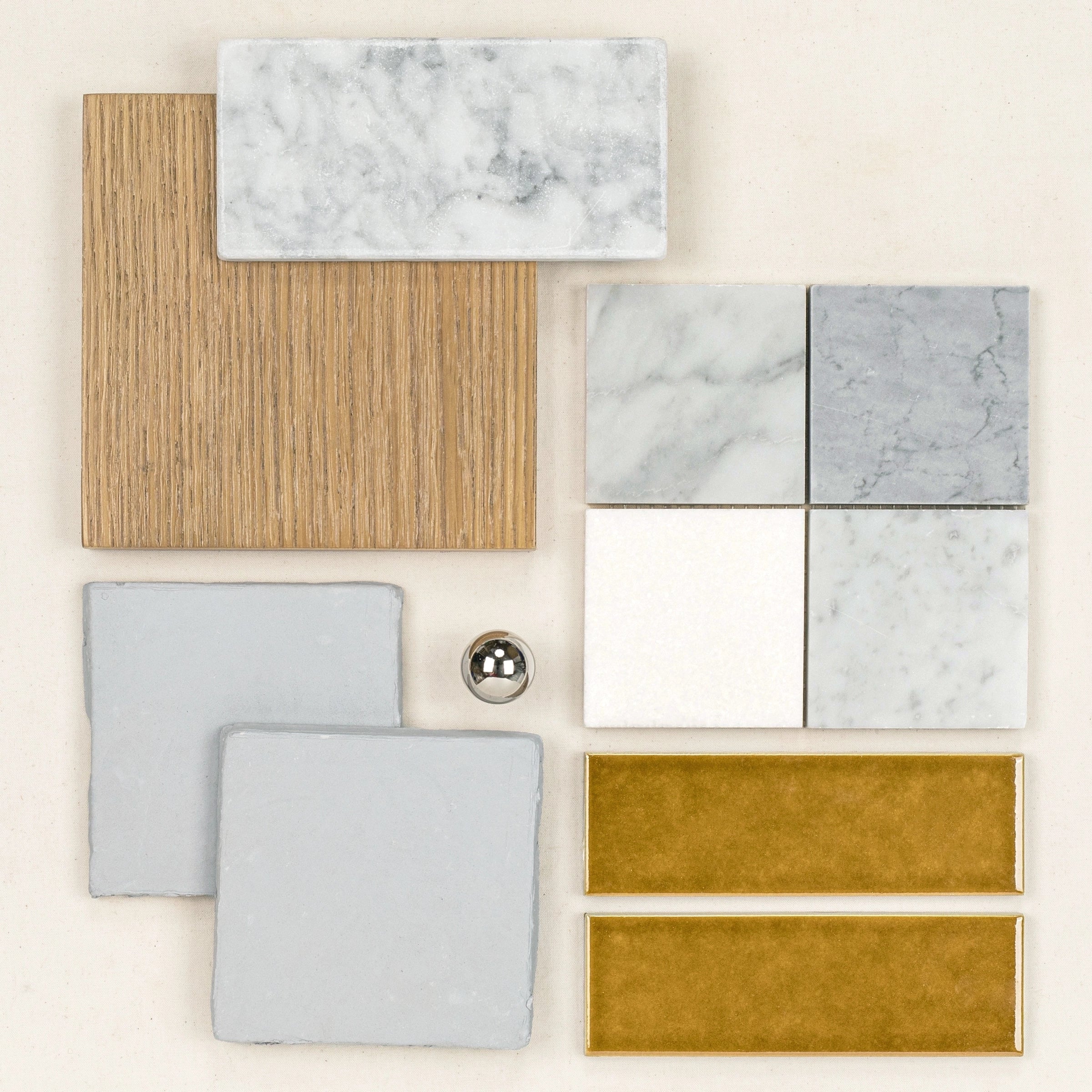 Flat lay of assorted ceramic and marble tiles in neutral tones, wood texture sample, and a small metallic sphere on a beige background