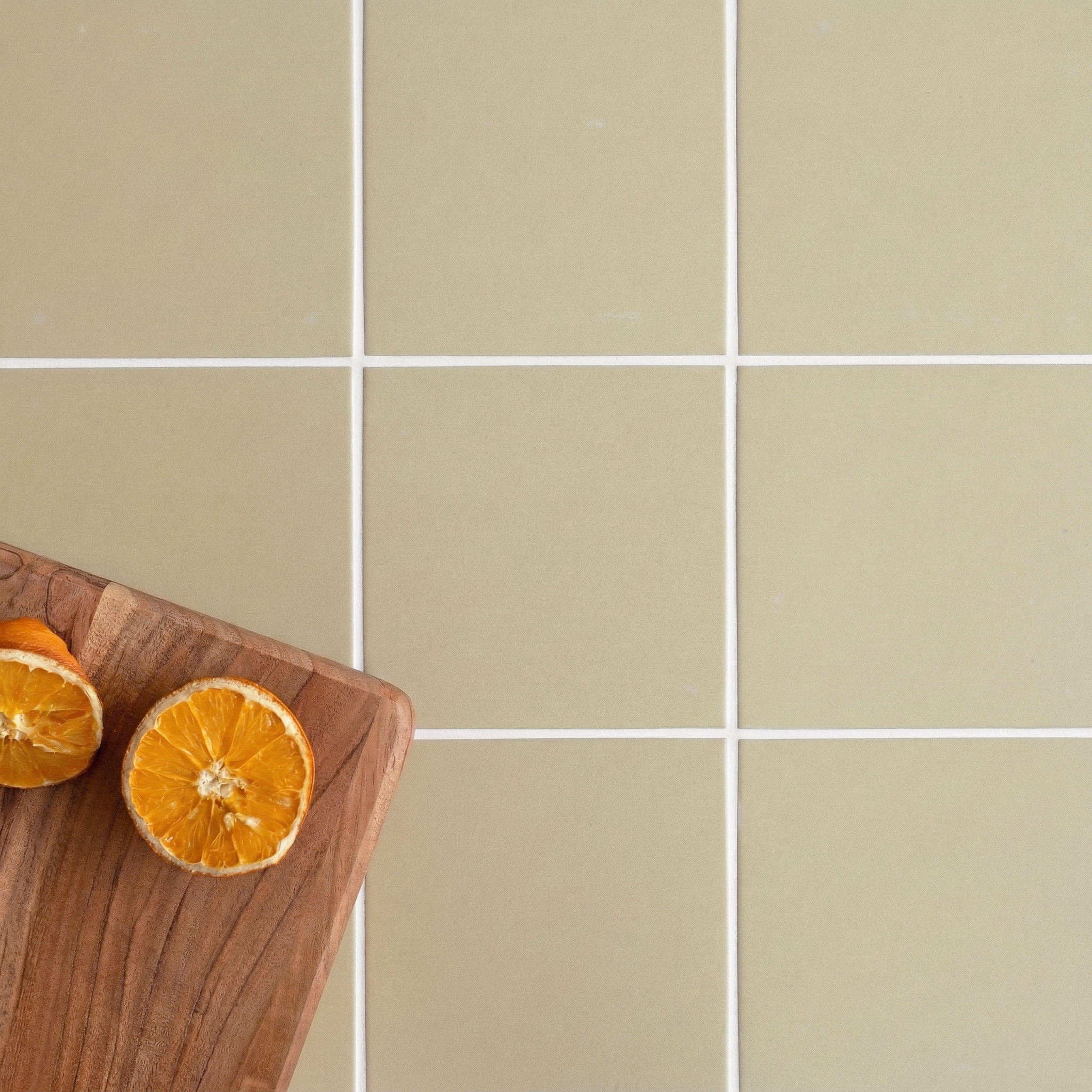 Close-up of beige ceramic tile flooring with white grout and a wooden cutting board holding halved dried oranges