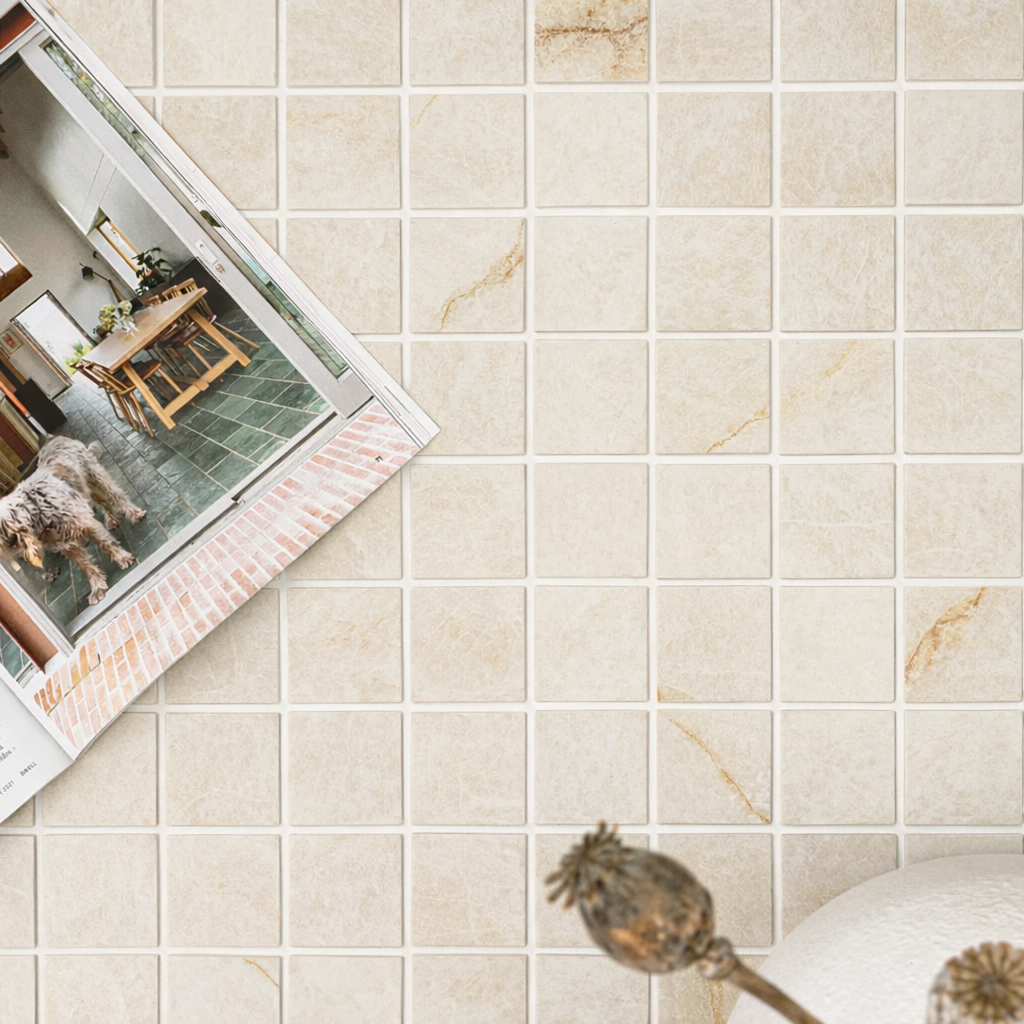 Creamy beige square tiles with subtle veining next to an open magazine and dried floral arrangement on light surface