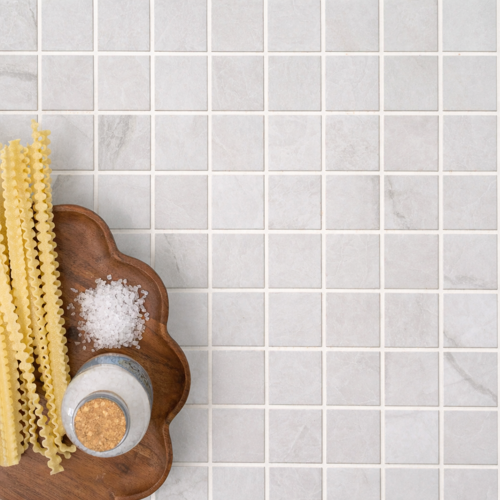Light grey square porcelain tiles with subtle texture beside wooden board holding dry pasta and coarse salt