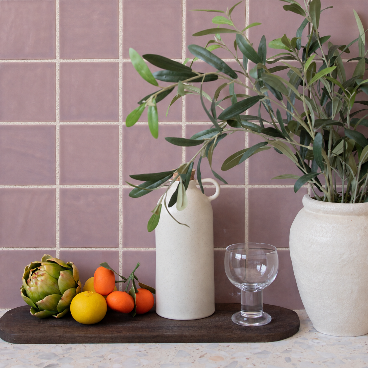 Mauve square tile backsplash with leafy branches, ceramic vases, citrus fruit, artichoke and wine glass