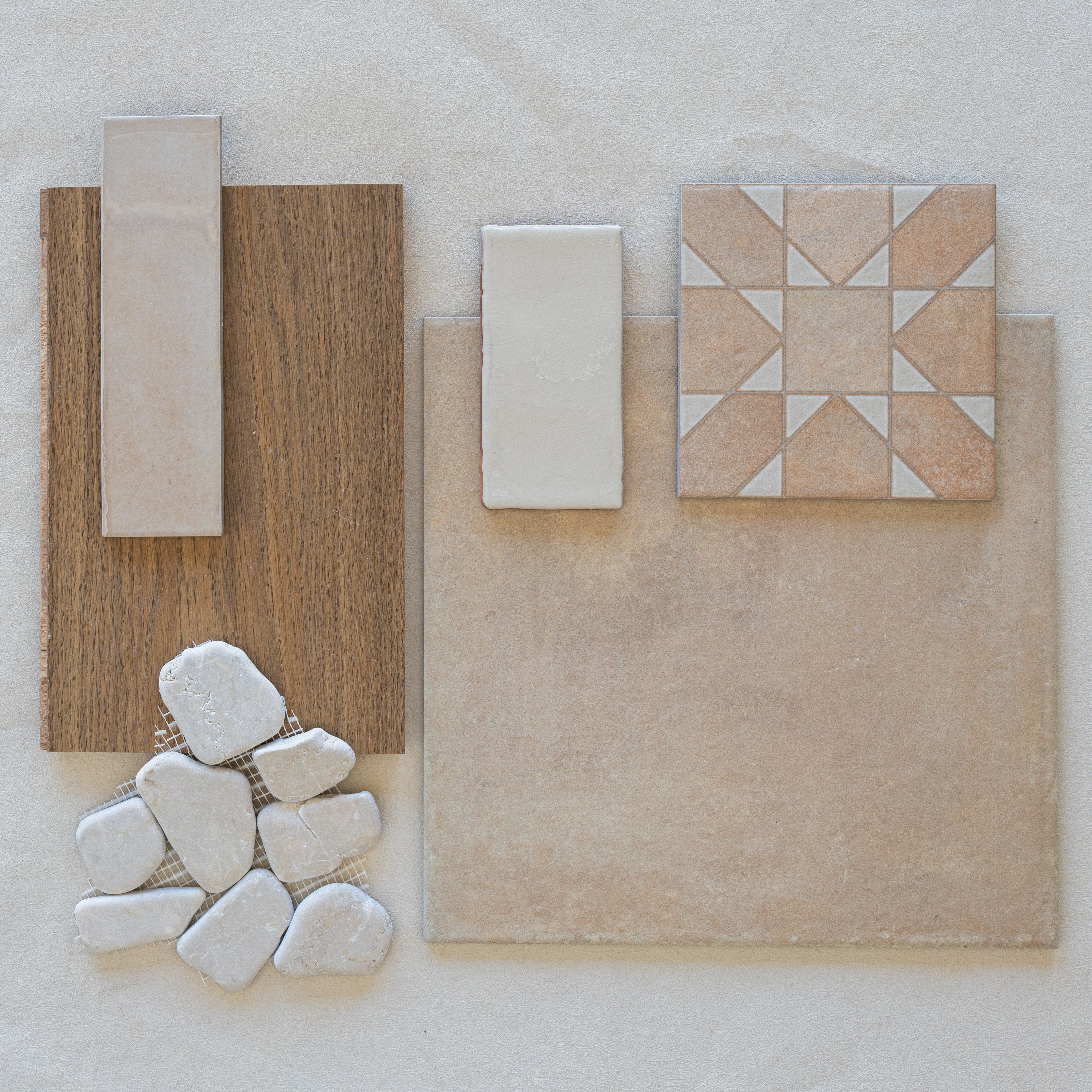 Assortment of ceramic tiles, natural stone pieces, and wood flooring samples in neutral beige and warm brown tones arranged on a light surface