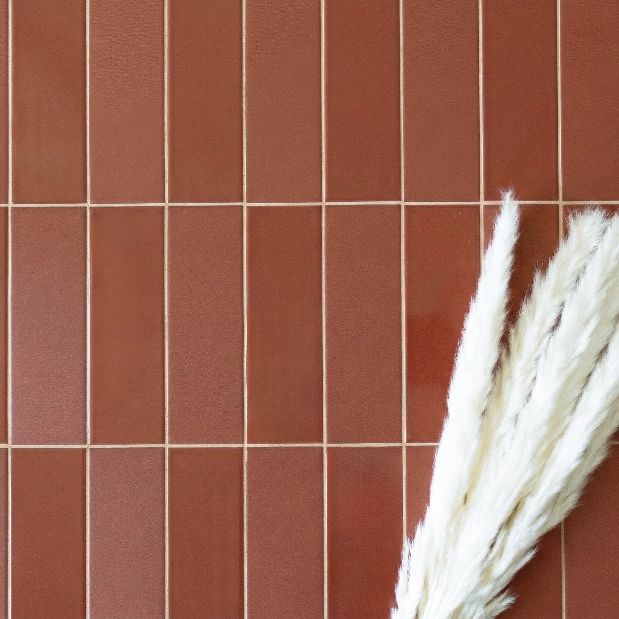 Grid of narrow rectangular porcelain tiles in warm cinnamon beige with fine grout lines and soft white pampas grass detail