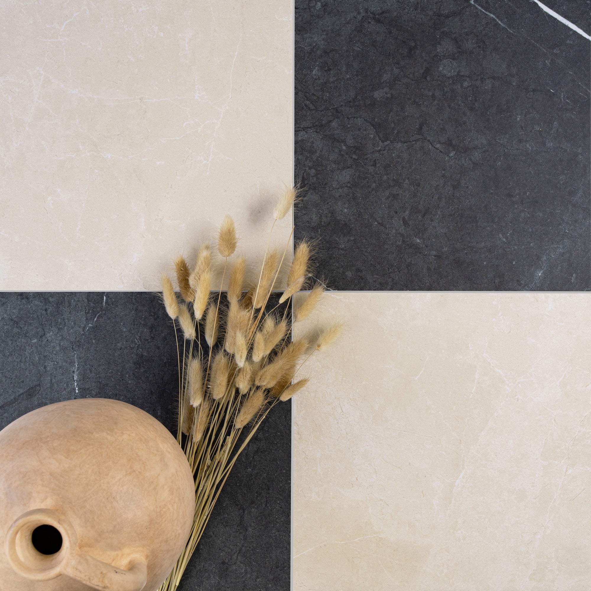Checkerboard pattern of large square tiles in cream and dark charcoal with marble-like veining and dried grasses nearby
